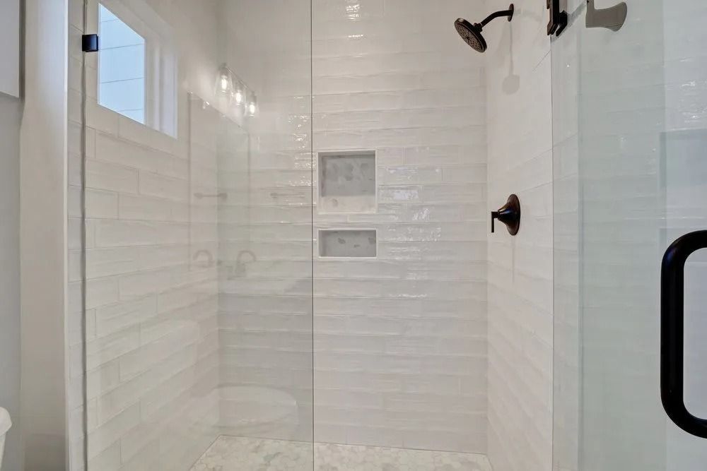Glass-enclosed shower with white textured tile walls, black fixtures, and built-in niches.