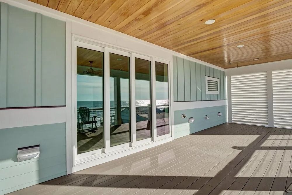 Covered deck with blue siding and sliding glass doors; wooden ceiling, and water view.