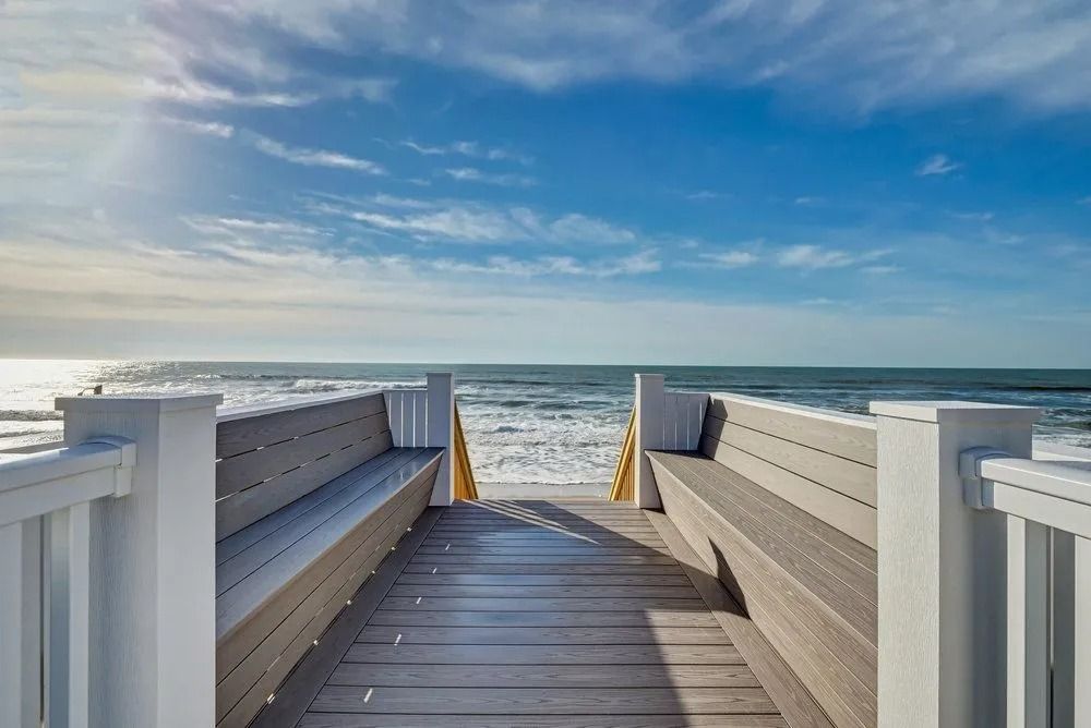 Wooden walkway with benches leading to the ocean under a blue sky.