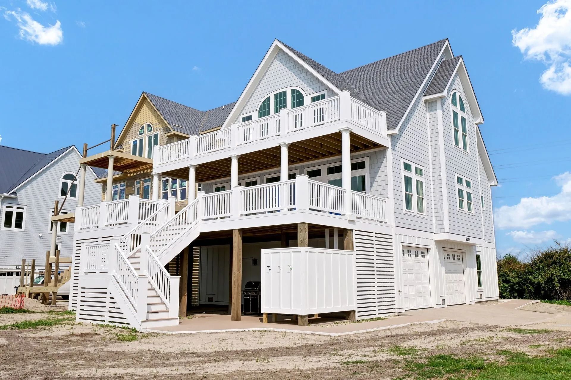Two-story beach house with light gray siding, white railings, and a balcony on a sunny day.