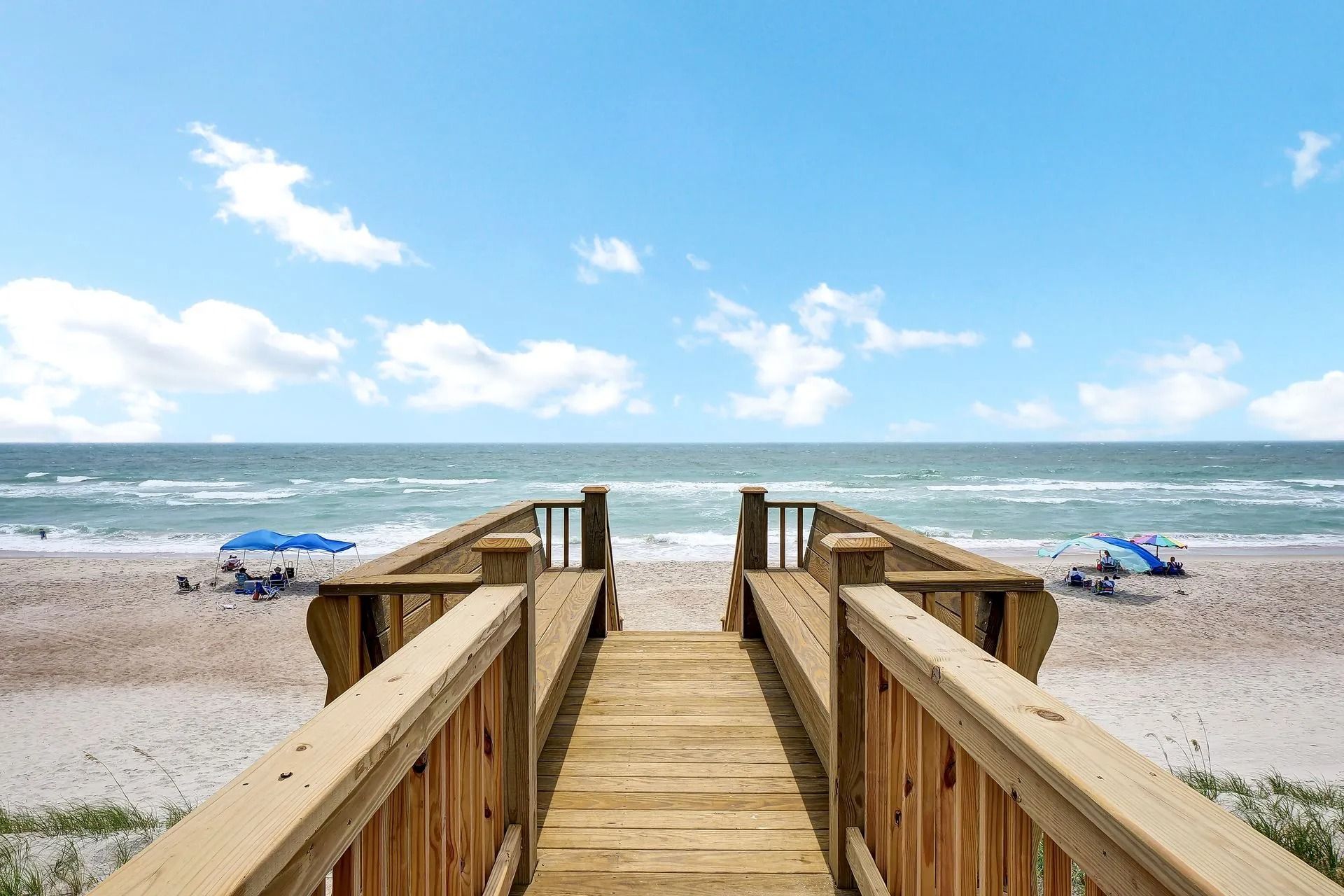 Wooden boardwalk leading to a beach, ocean, and blue sky.