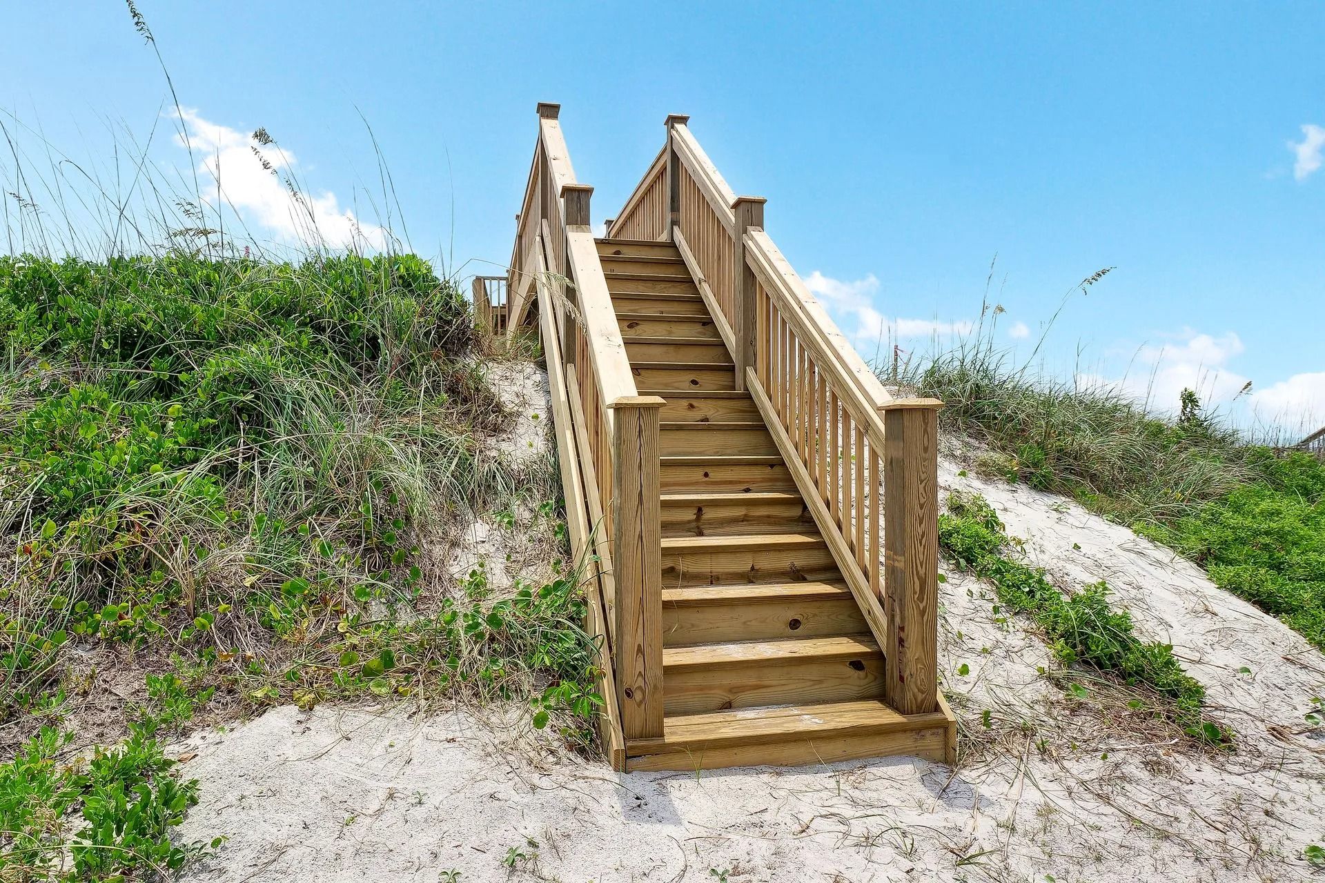 Wooden staircase on a sandy dune, leading to an unseen destination, blue sky in the background.