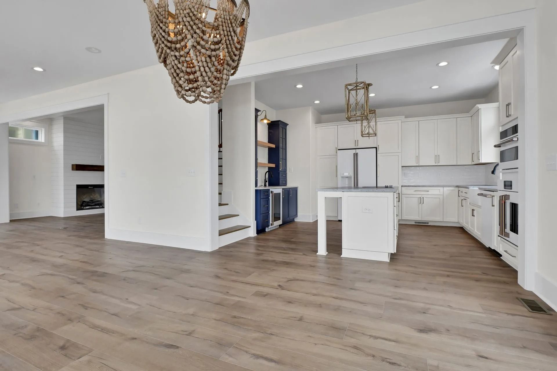 Spacious, modern kitchen with white cabinetry, island, and wood floors. Open to living area with fireplace.