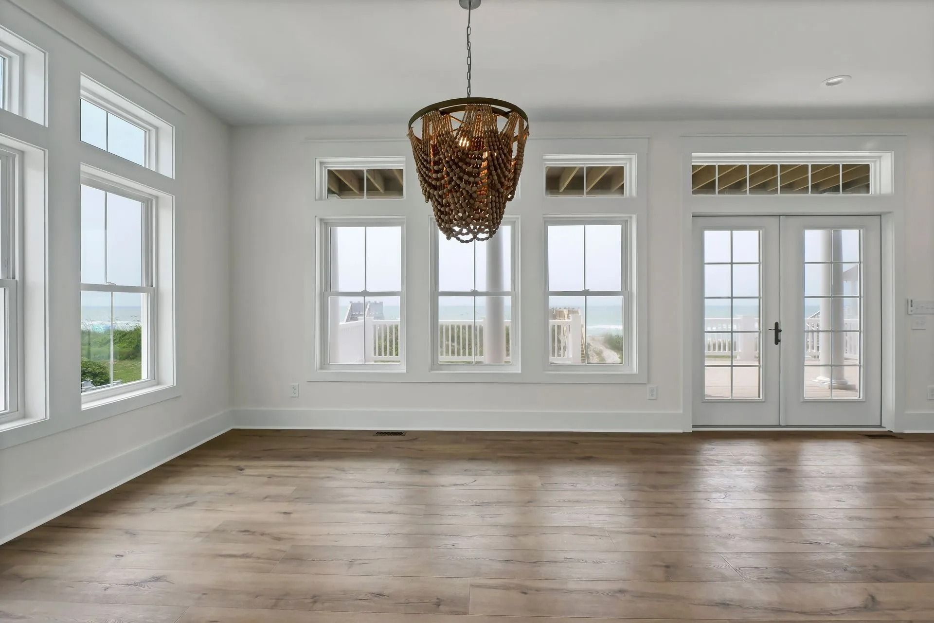 Empty room with wood floors, white walls, large windows overlooking a scenic view, and a decorative chandelier.