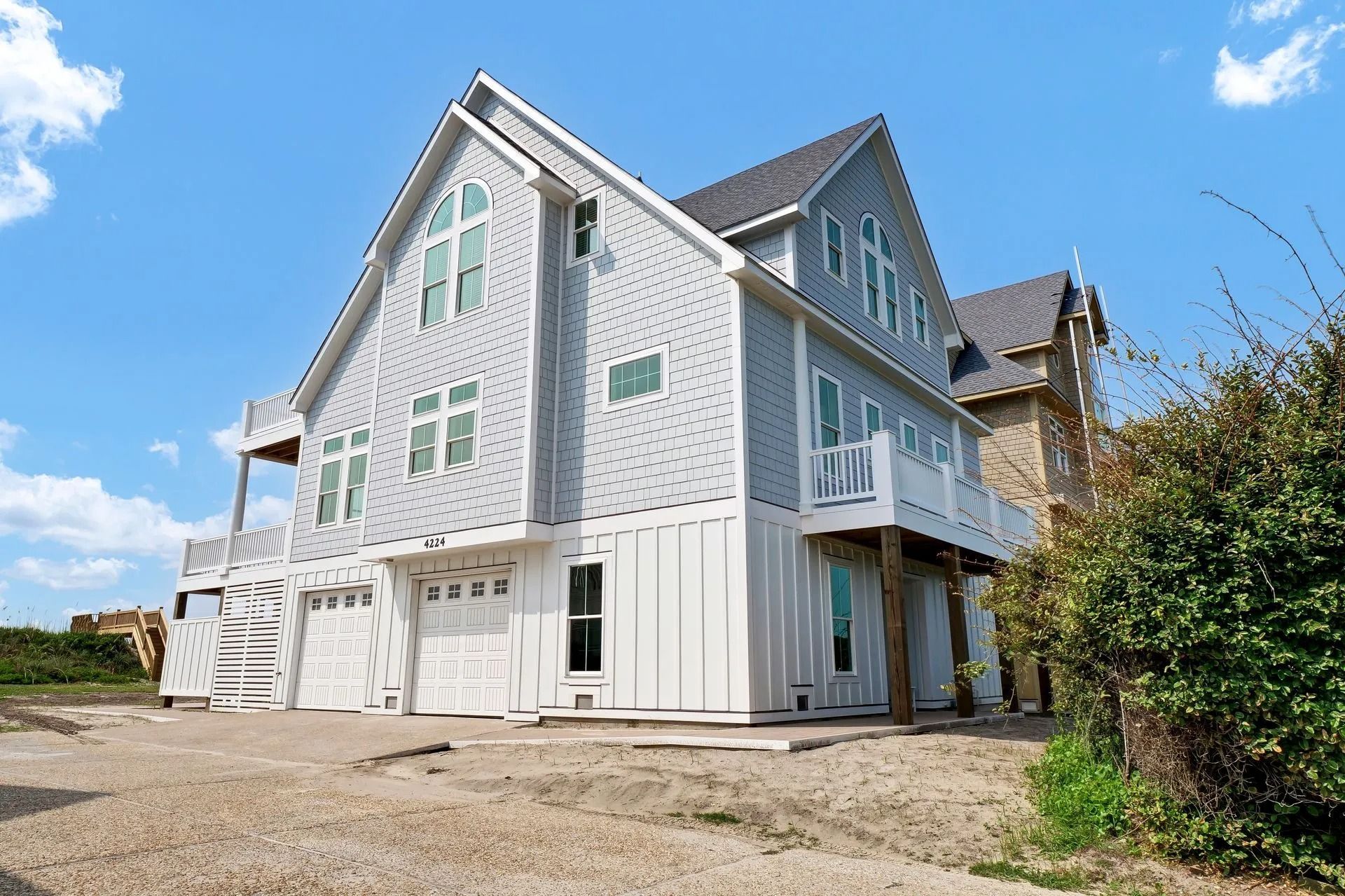 Two-story gray house with white trim, garage, balcony, and landscaping against a blue sky.