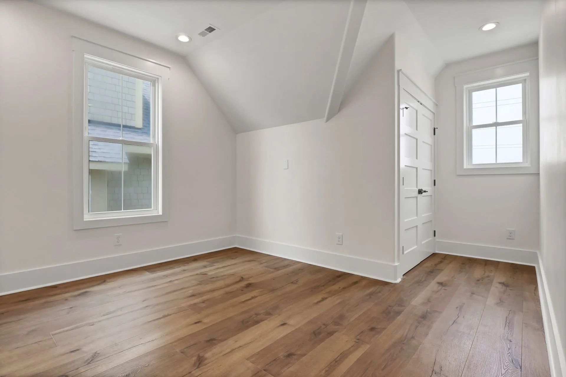 Empty room with wood floors, white walls, two windows, and a door.