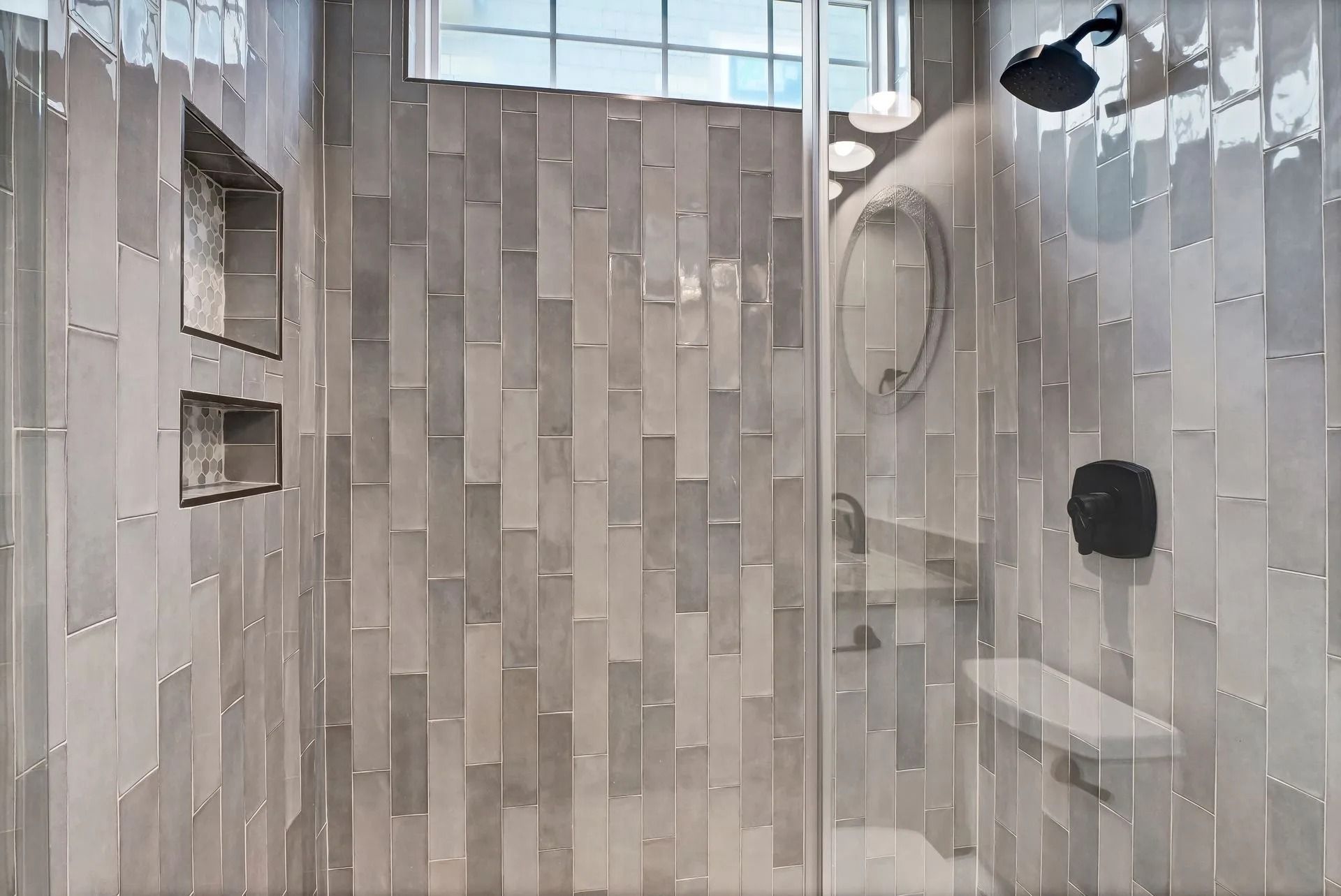 Shower interior with gray, vertical tiles, a glass door, and a built-in bench.