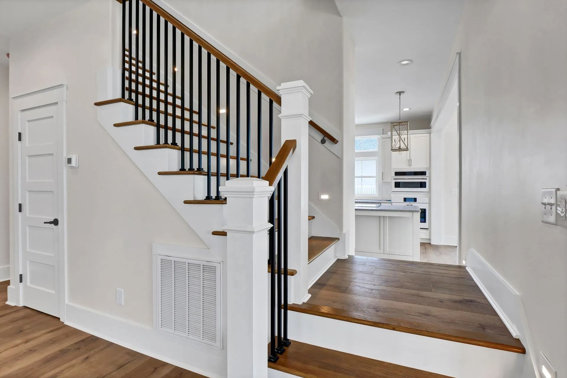 Staircase with wooden steps and black railings, leading to a kitchen with white cabinets.