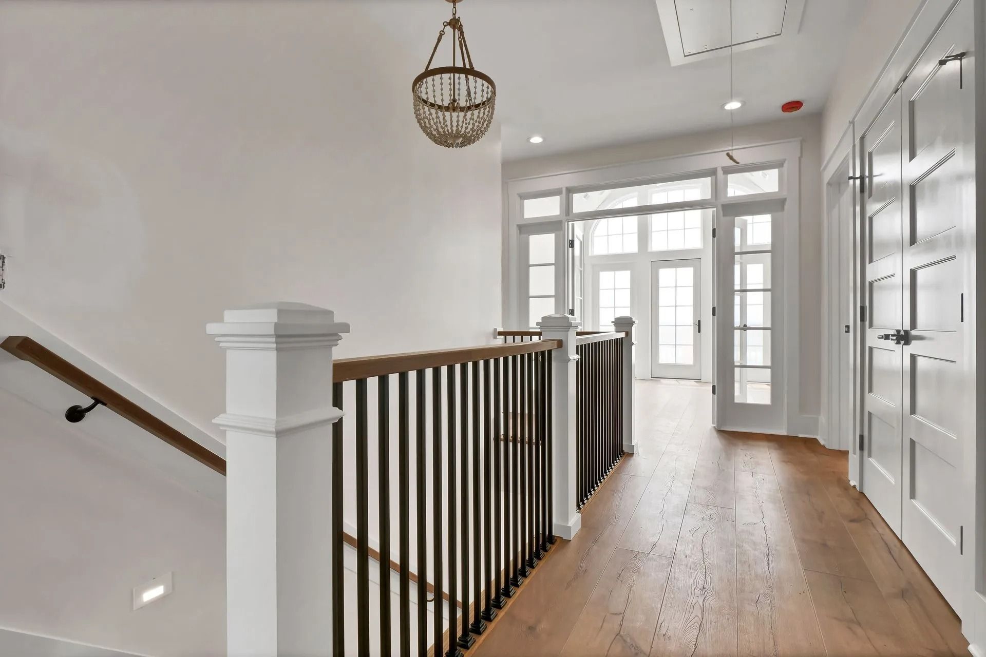 Hallway with stairs and doorway. White walls, wooden floors, and a decorative light fixture.