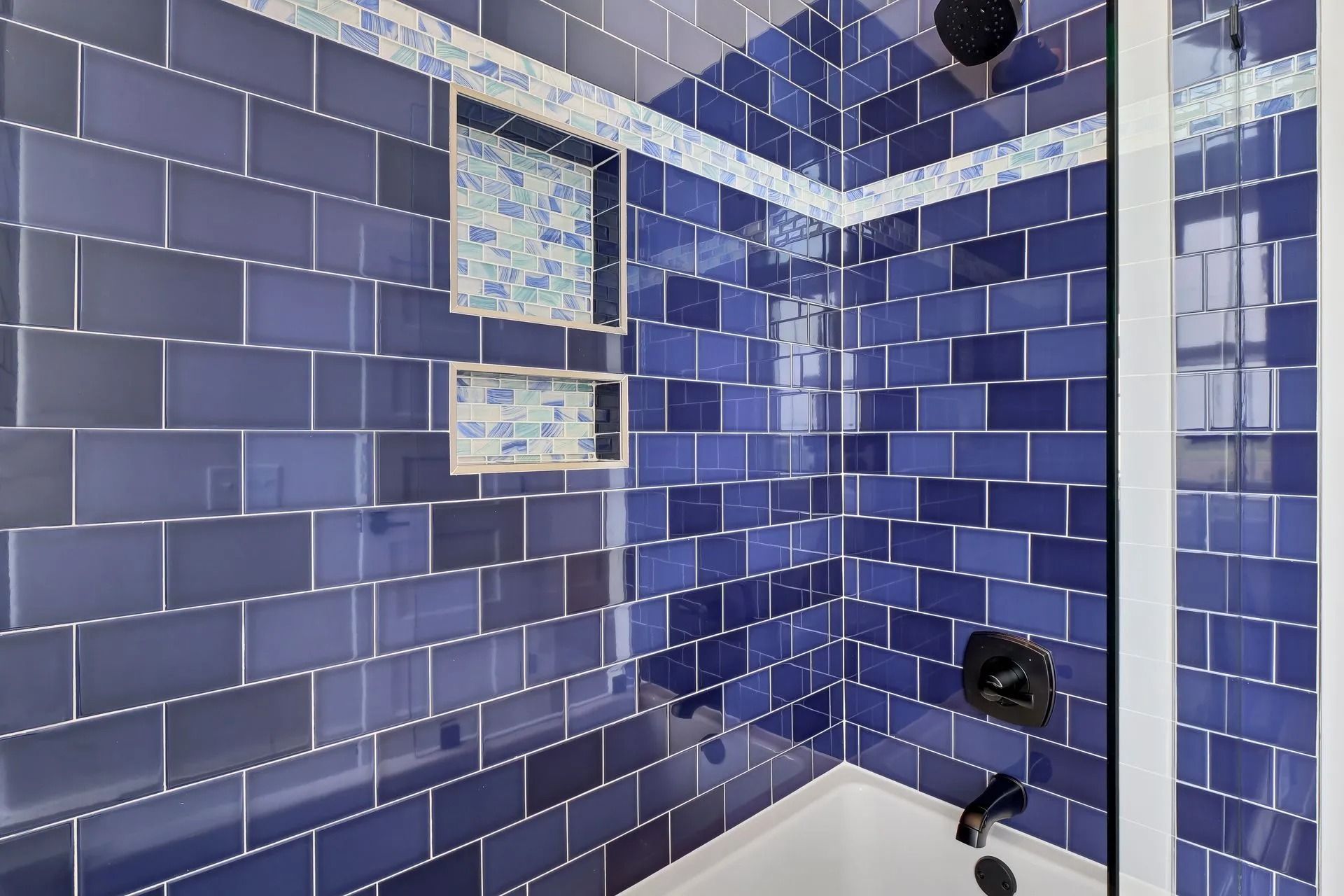 Blue tiled shower with built-in shelves and black fixtures.