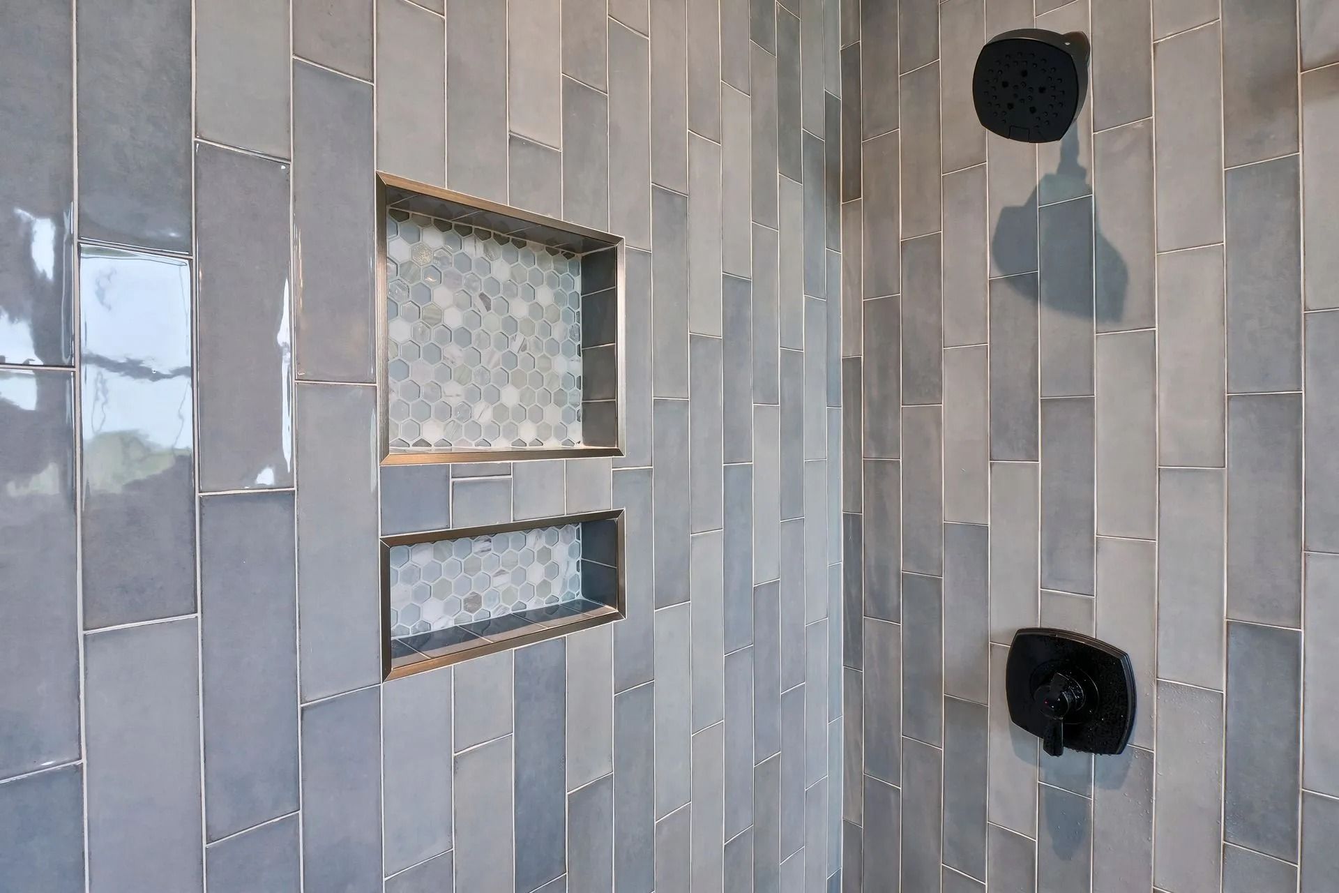 Gray tiled shower with two built-in niches and black fixtures.