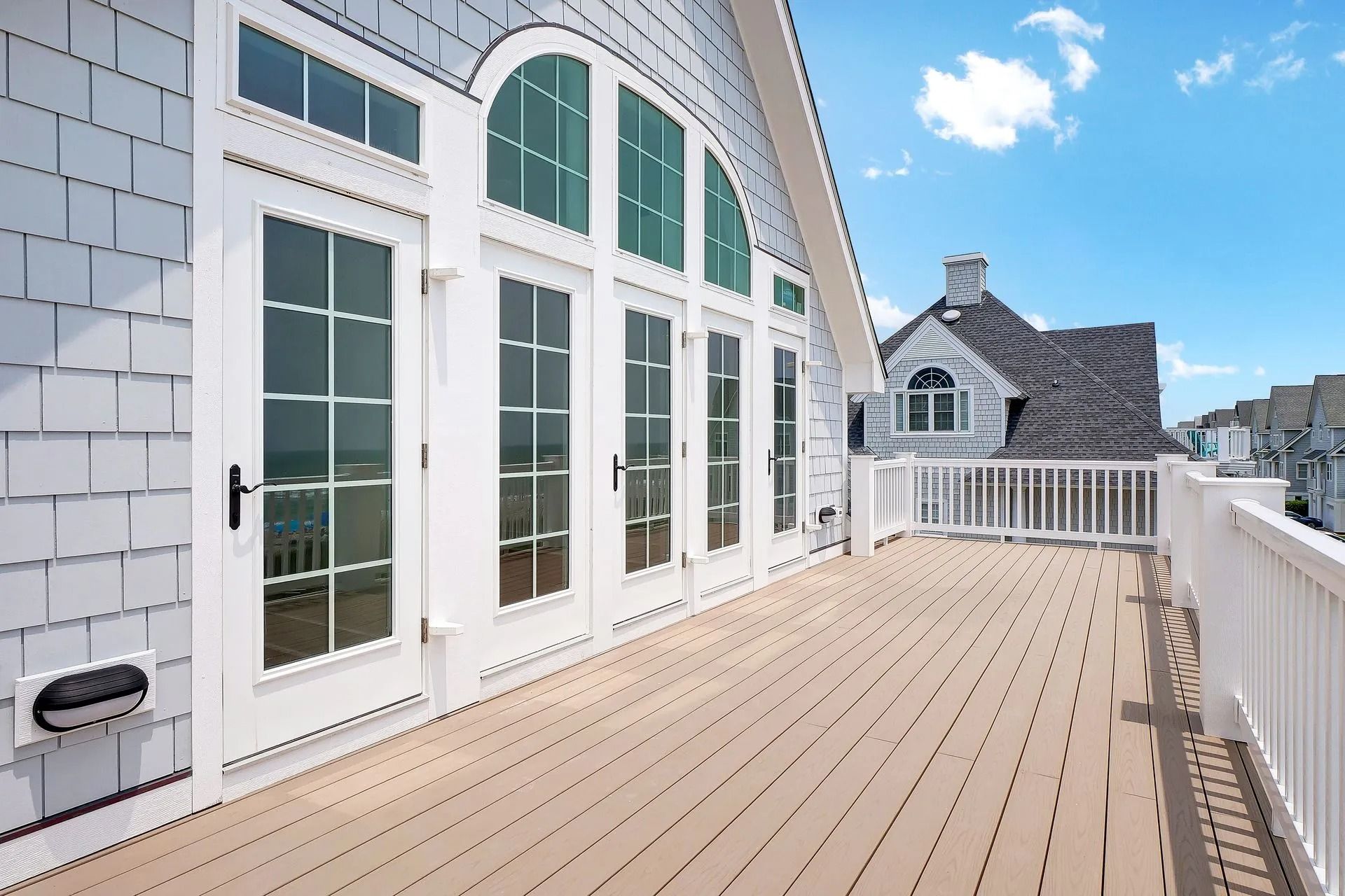 Deck with white railing and doors, shingled wall, and sunny blue sky.