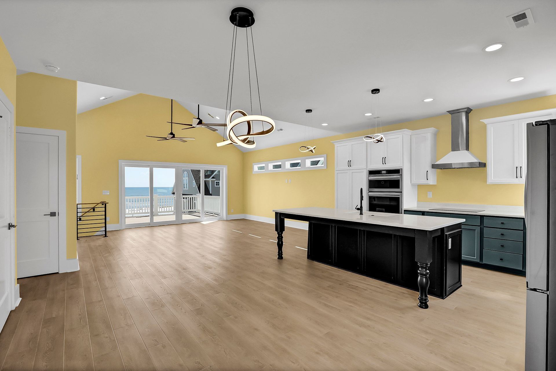 Open-concept kitchen with light wood floors, island, and blue cabinets, with view of ocean through sliding glass doors.