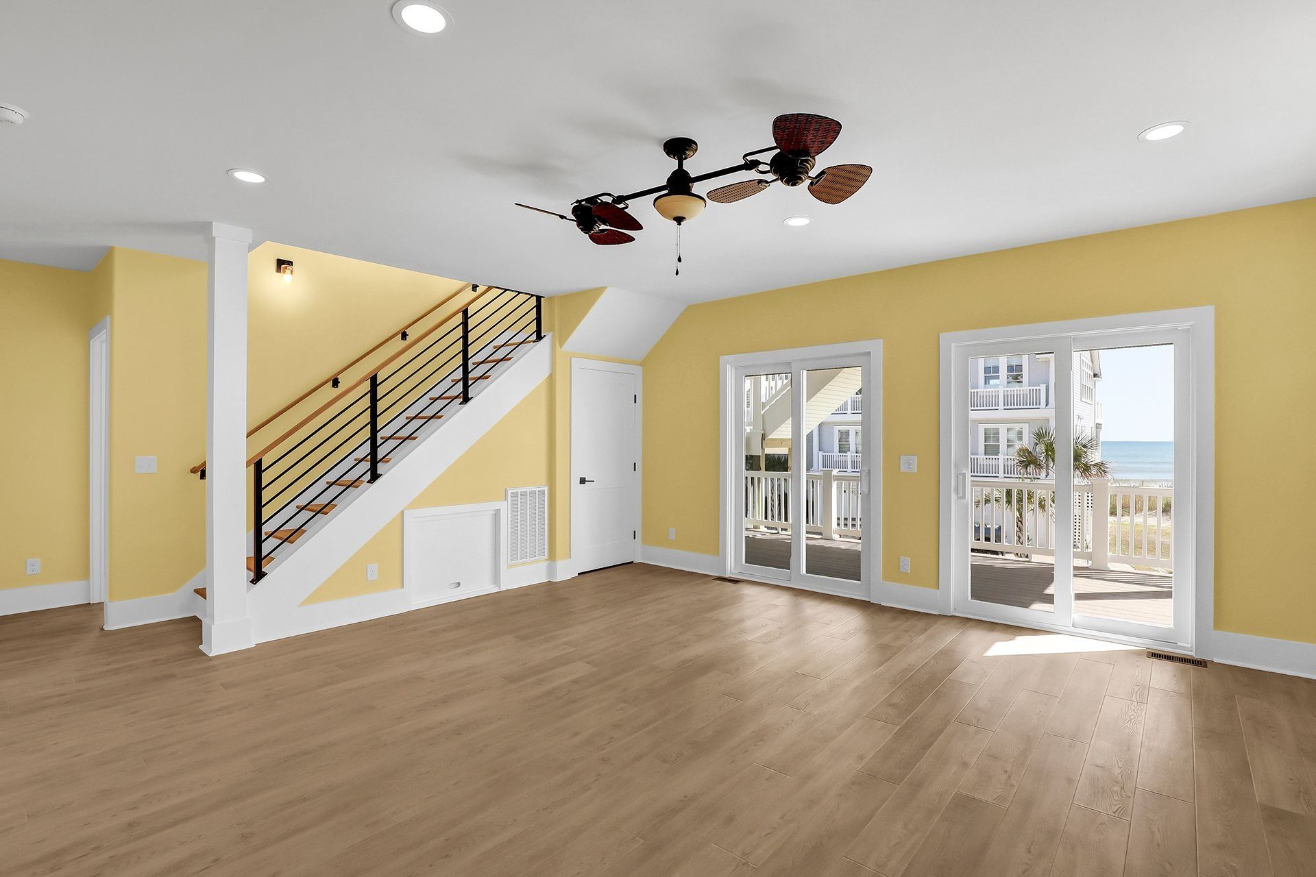 Spacious room with stairs and beach access, yellow walls, wood floors, and ceiling fan.
