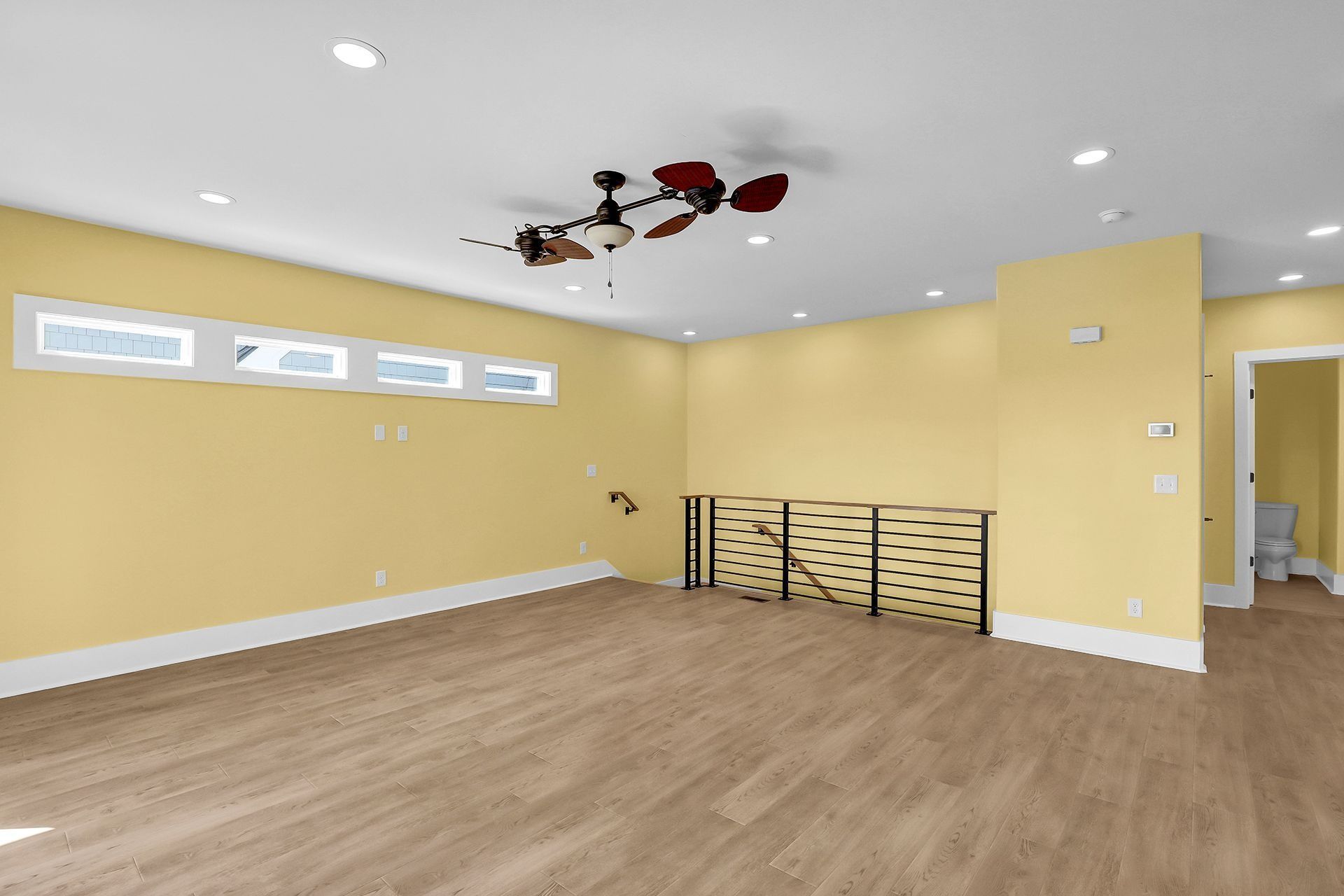 Empty room with light yellow walls, wood flooring, and a decorative railing.