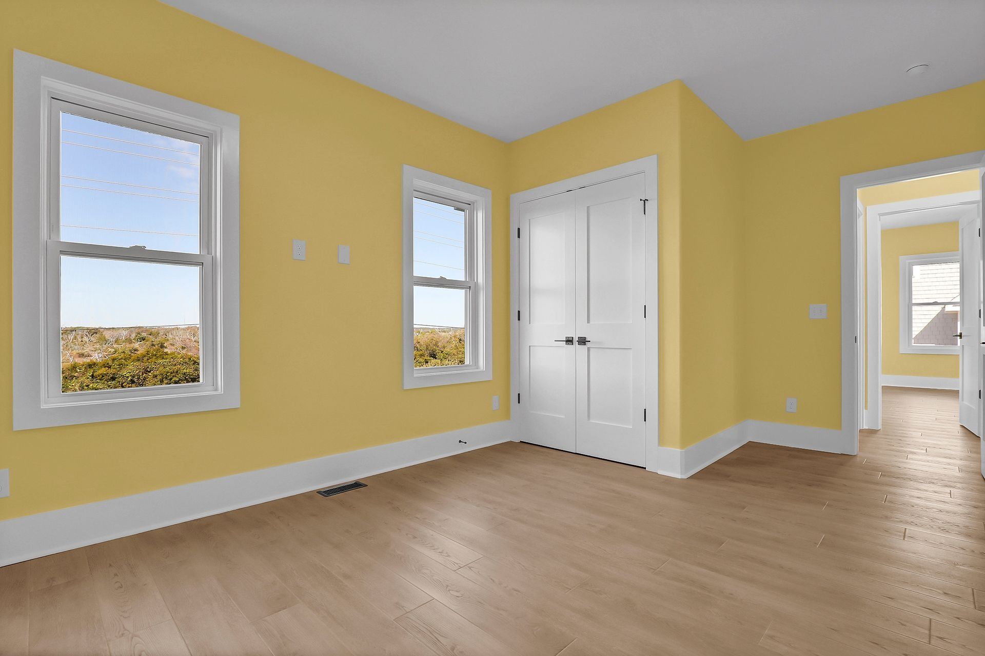 Empty room with yellow walls, white trim, two windows, a double door, and wood floor.