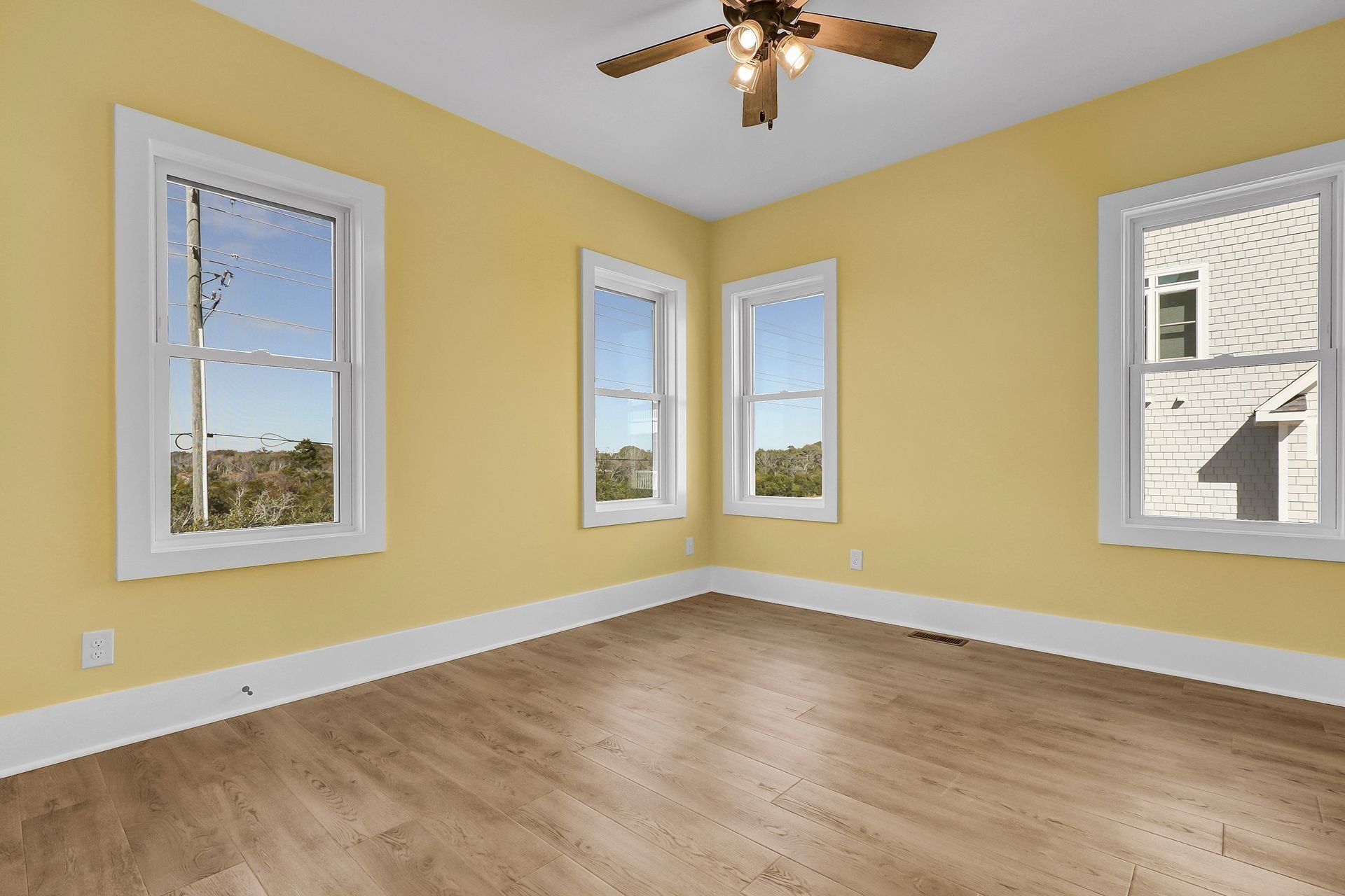 Empty room with yellow walls, white trim, wood floor, and three windows.