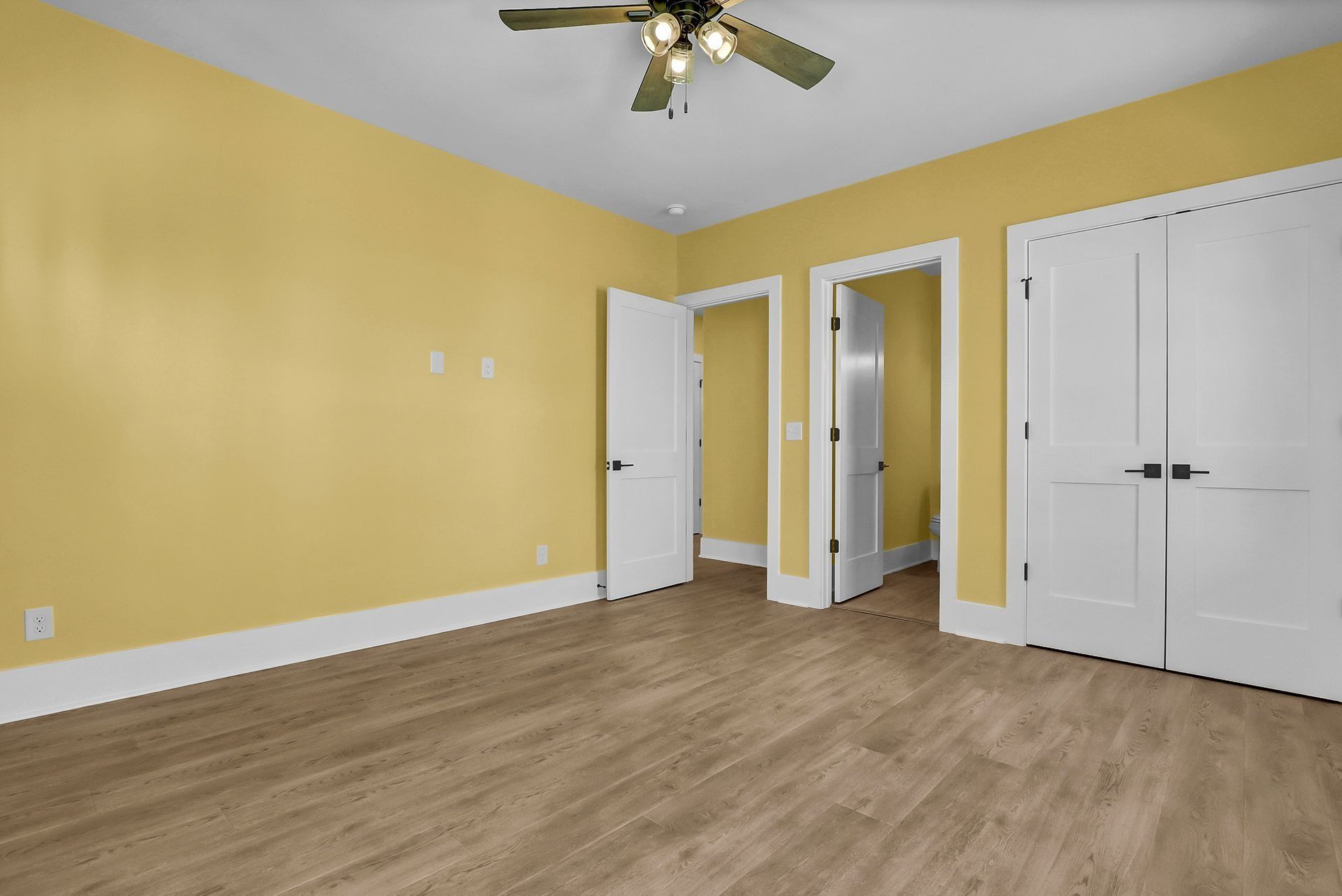 Empty room with yellow walls, hardwood floors, white doors, and a ceiling fan.