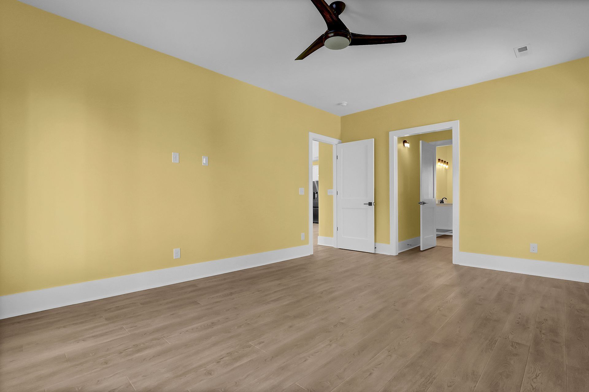 Empty room with yellow walls, white trim, and a ceiling fan. Light wood-look flooring.