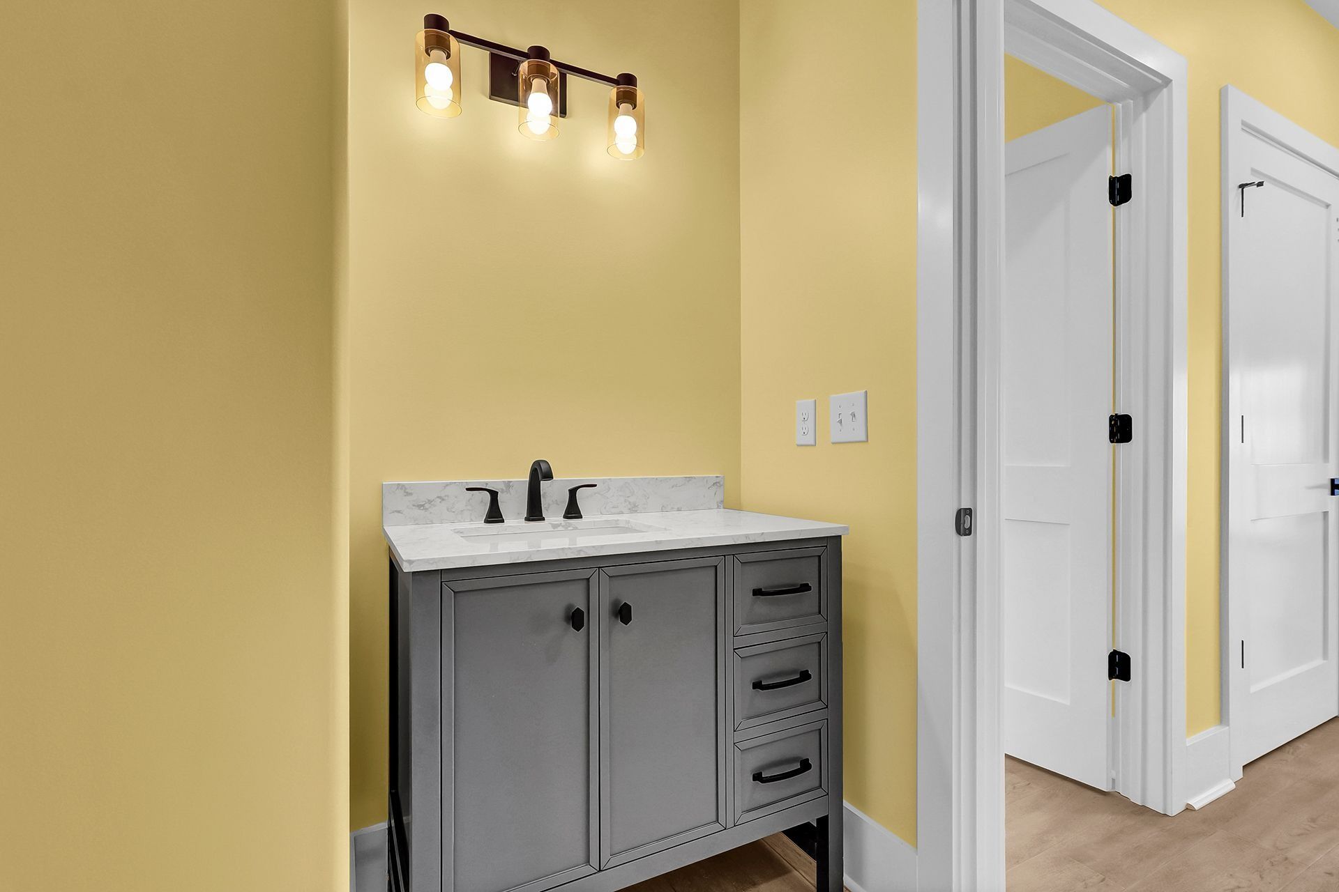 A bathroom with gray vanity, white countertop, and yellow walls. Two white doors lead to other rooms.