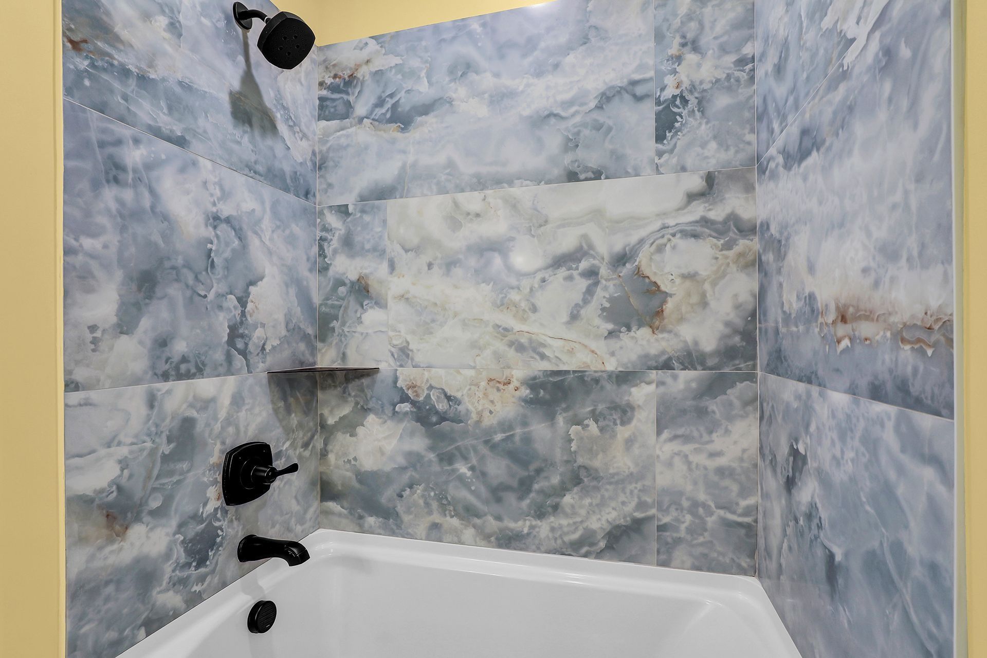 Blue marble-tiled shower with black fixtures; white bathtub, showerhead, and a shelf.