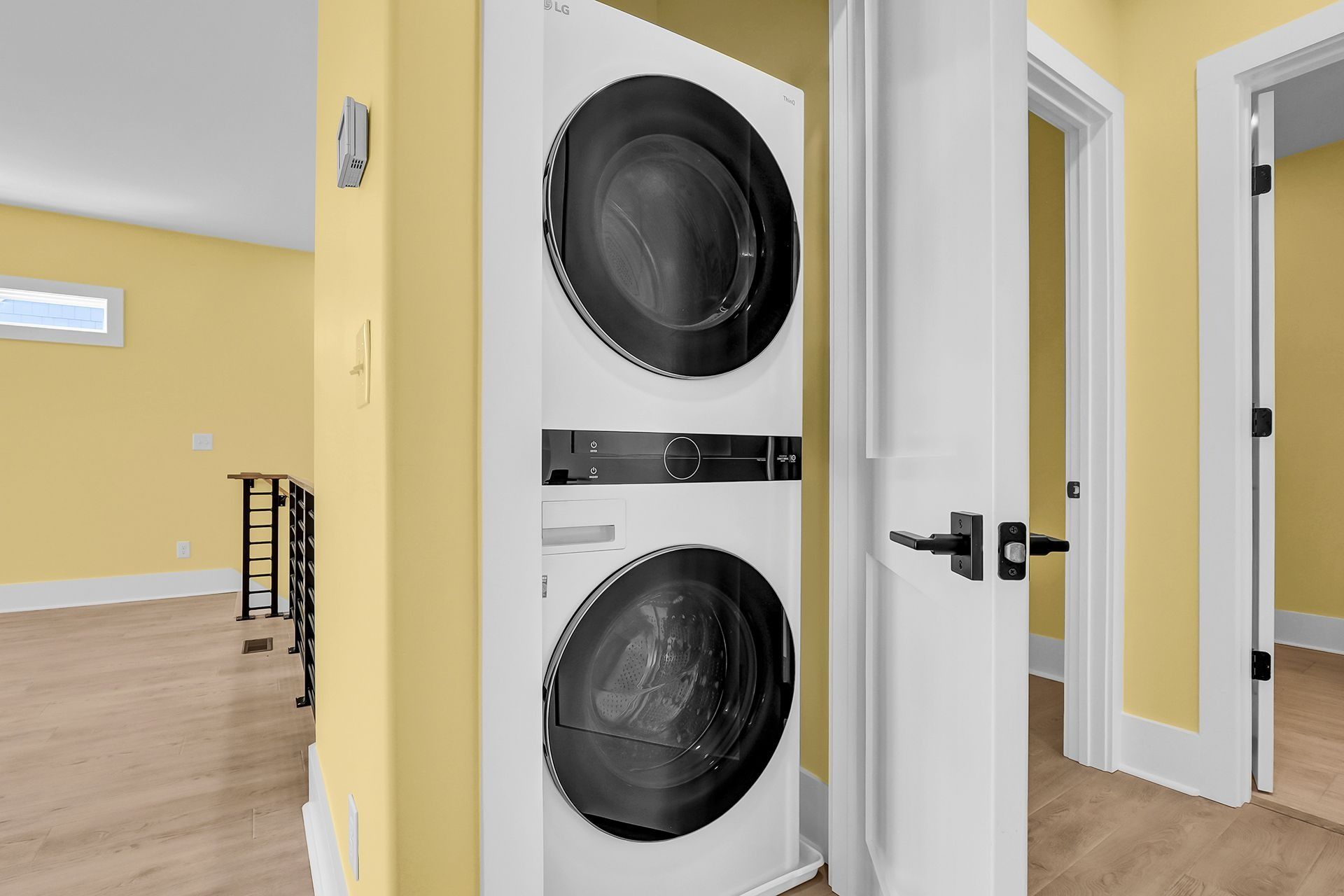 Stacked white washer and dryer in a yellow-painted laundry area, near a doorway.