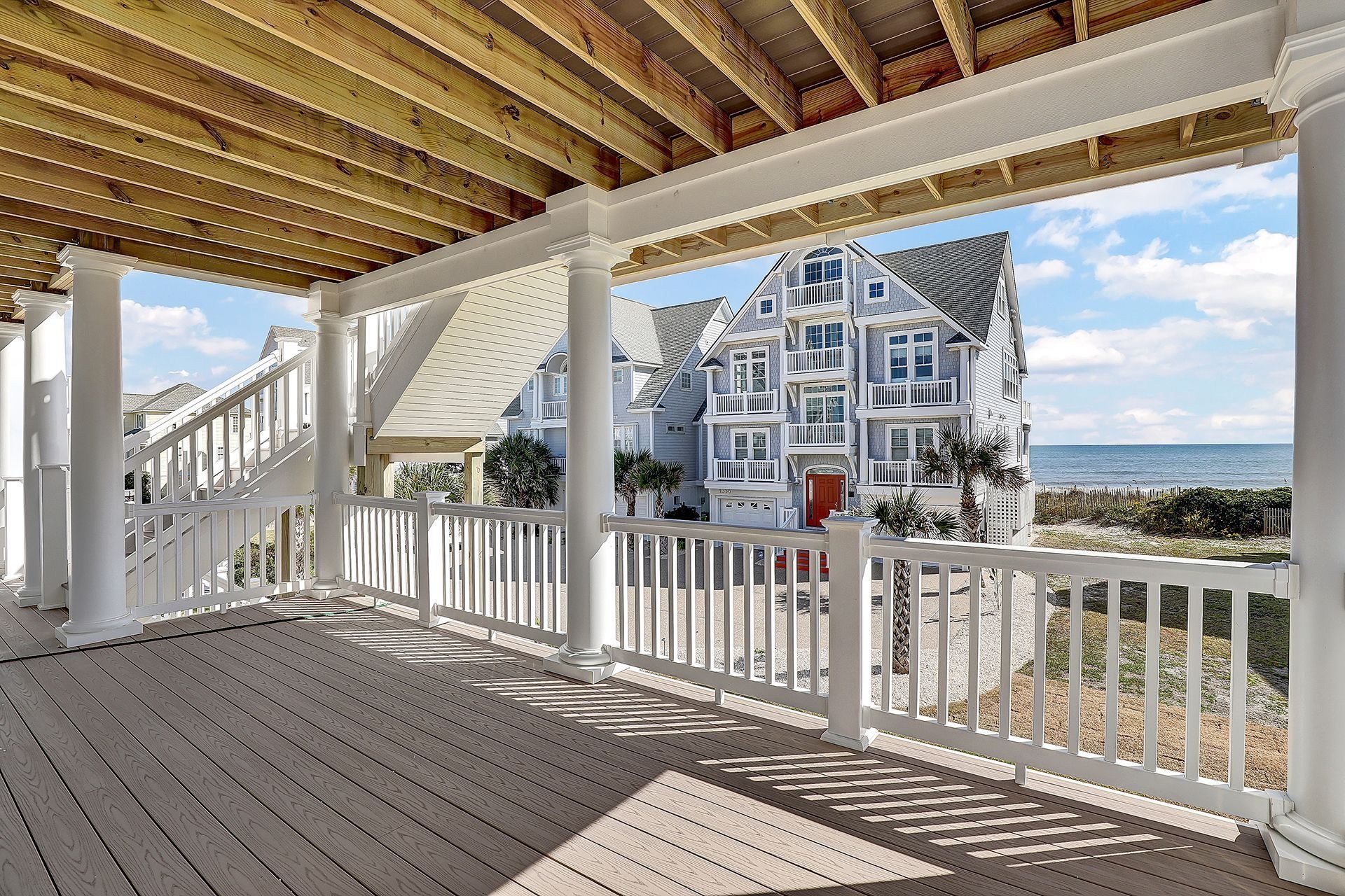 Oceanfront porch with white railings and columns, view of a light blue house.