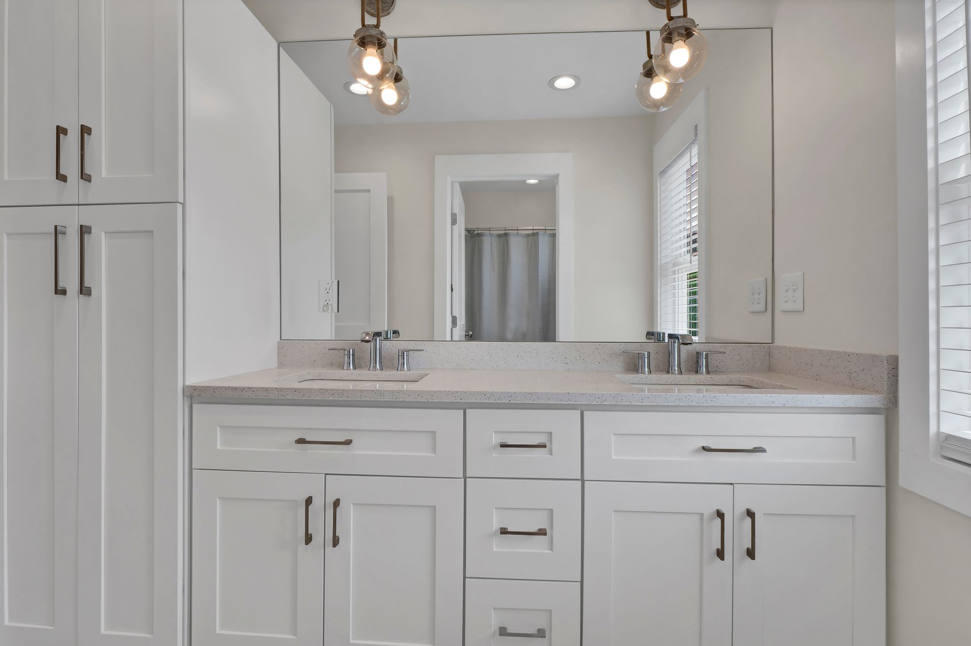 White bathroom with double vanity, large mirror, and overhead lights.