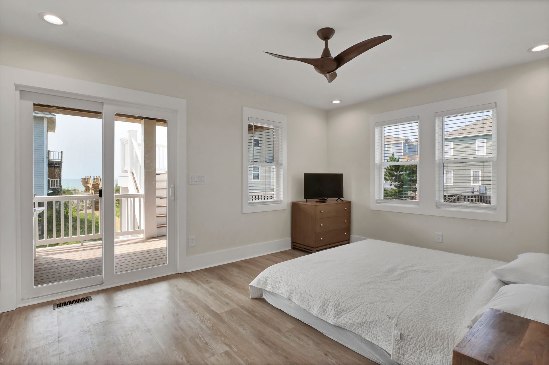 Bedroom with sliding door to balcony, hardwood floors, bed, dresser, windows, ceiling fan.