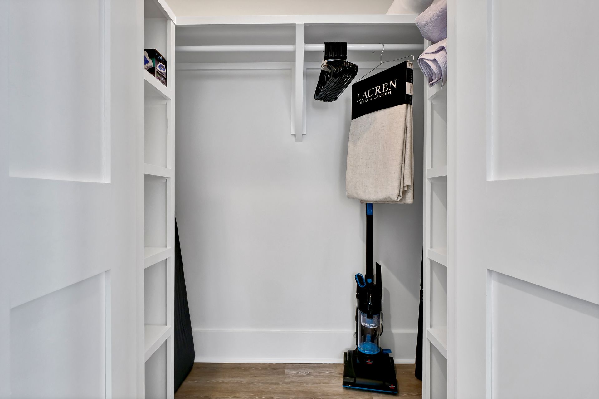 White closet with shelves, a vacuum, and hanging items.