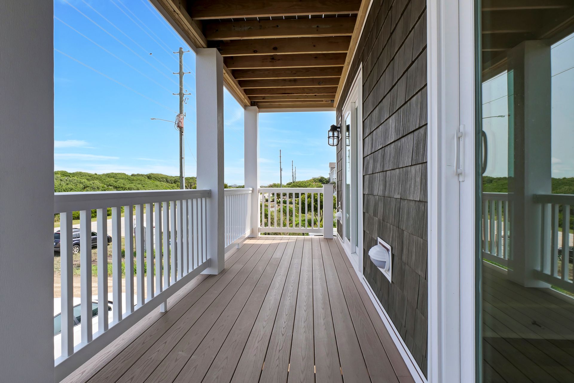 Wooden deck with white railing, wooden ceiling, and a view of trees and sky.