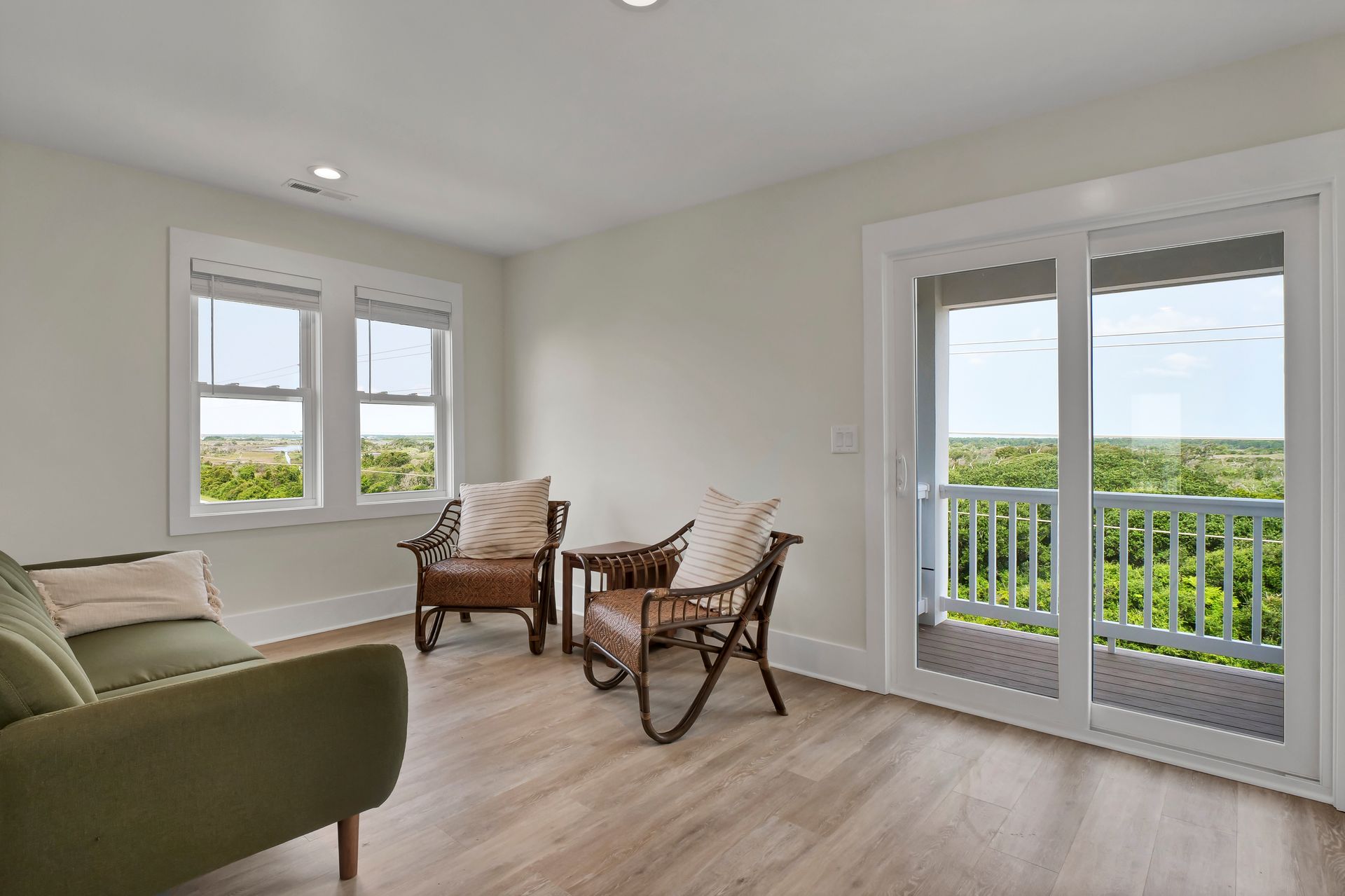 Living room with green sofa, two wicker chairs, and balcony view.