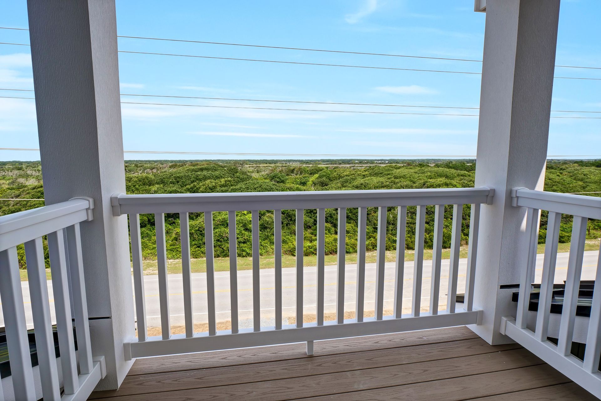 View from a white porch with railings overlooking a green landscape and blue sky.