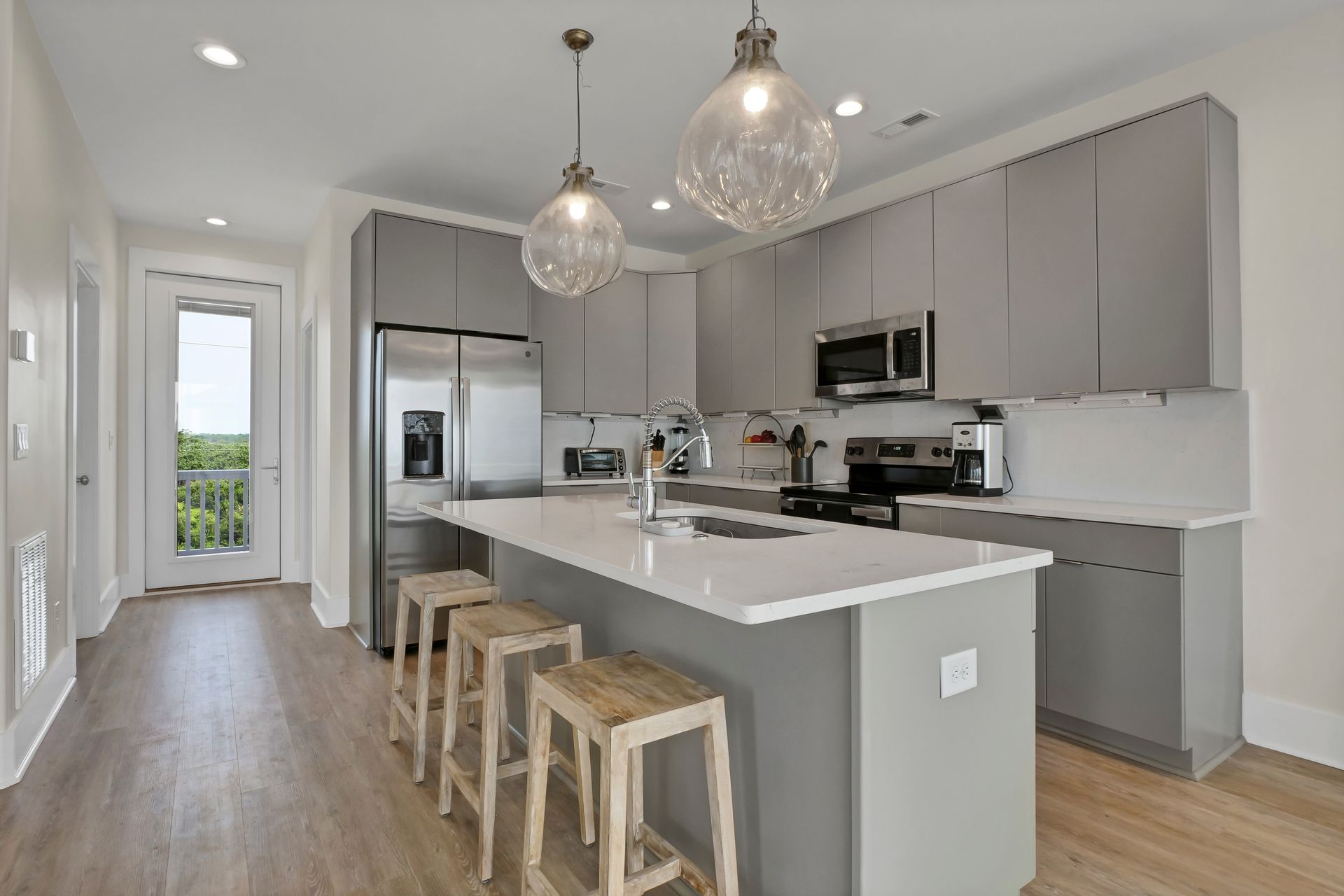 Modern kitchen with gray cabinets, white island, and wooden stools.