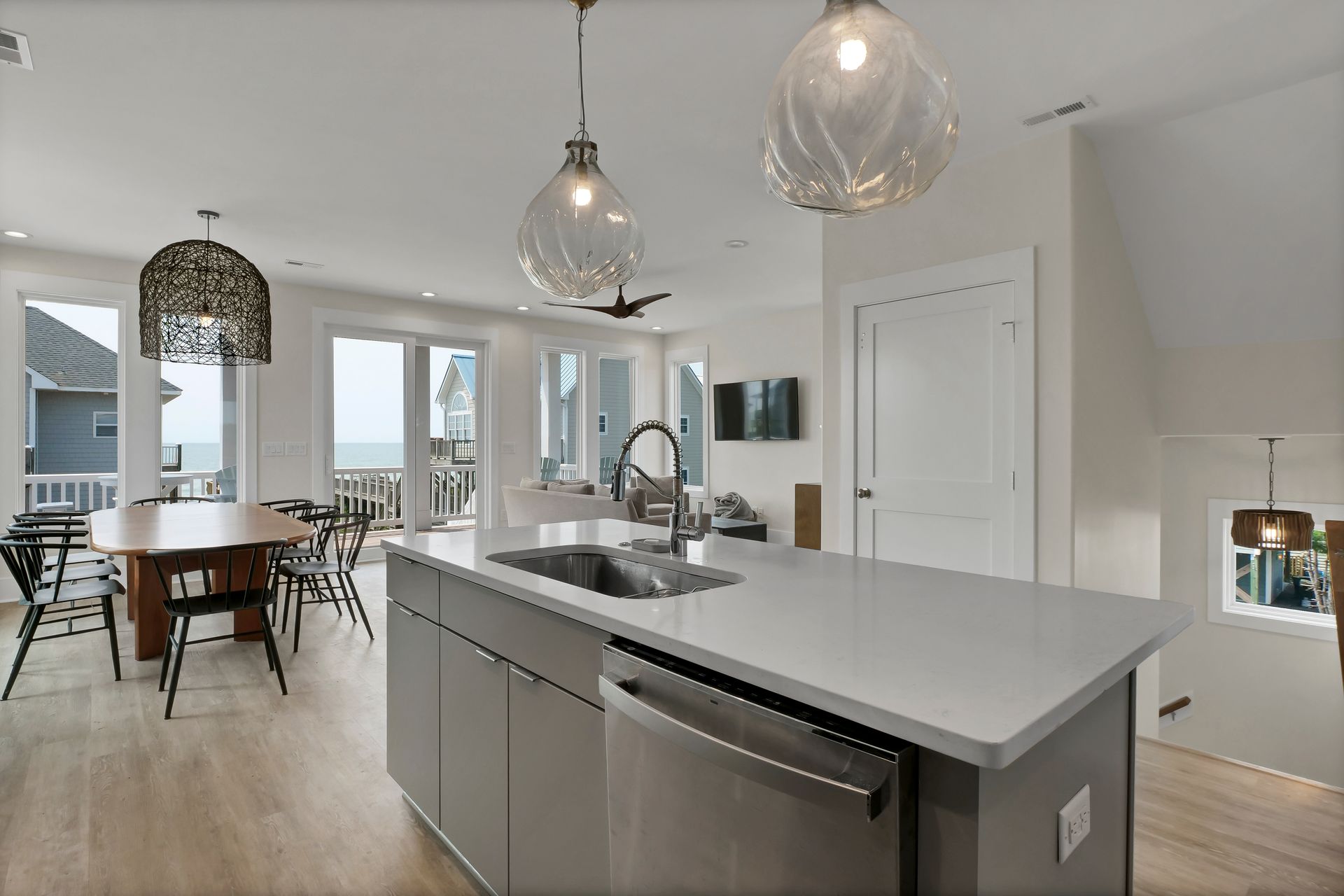 Modern kitchen with island, sink, and pendant lights; dining area with table and chairs; ocean view.