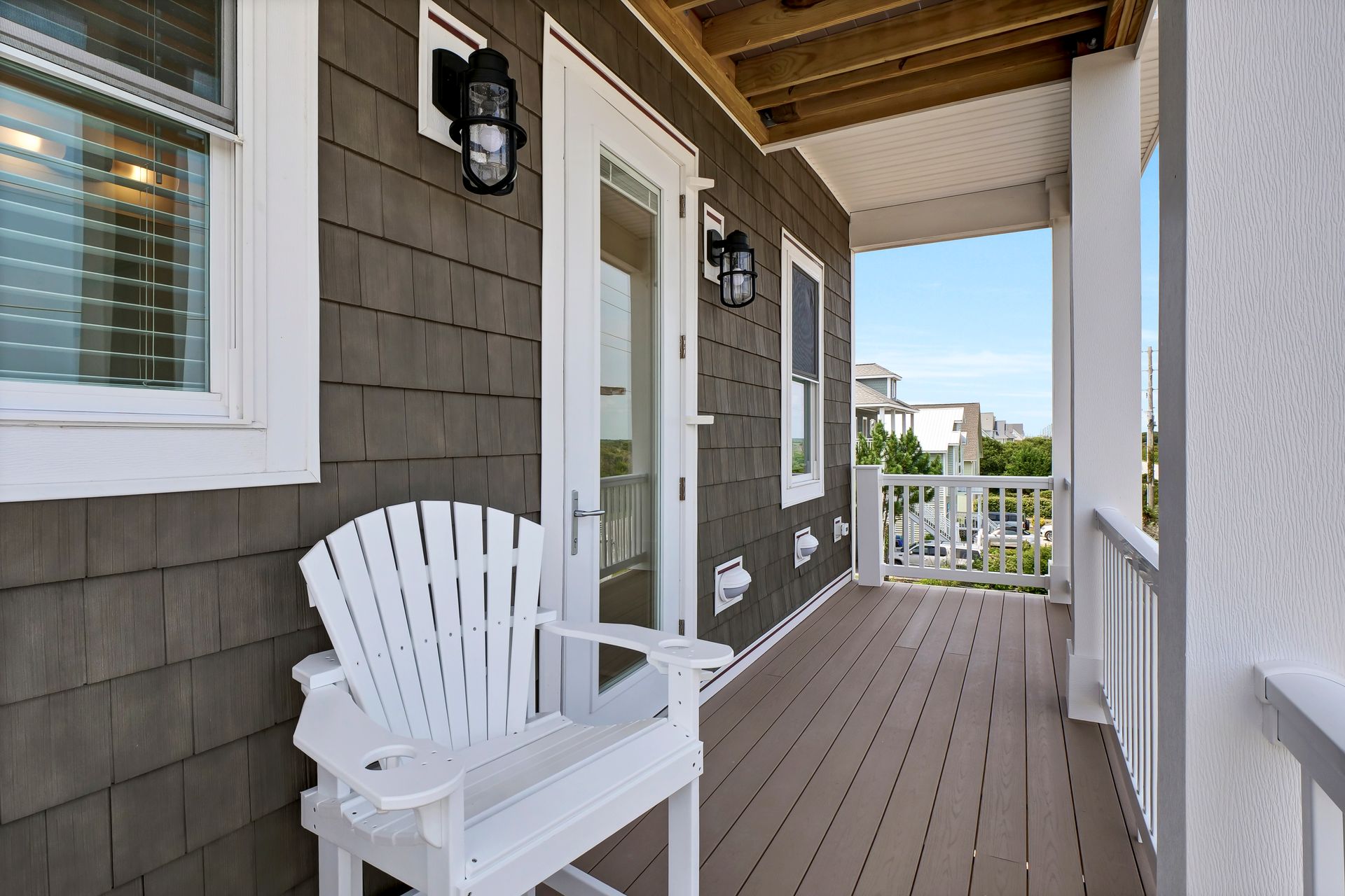 White Adirondack chair on a wooden porch with double doors and a view of the sky.