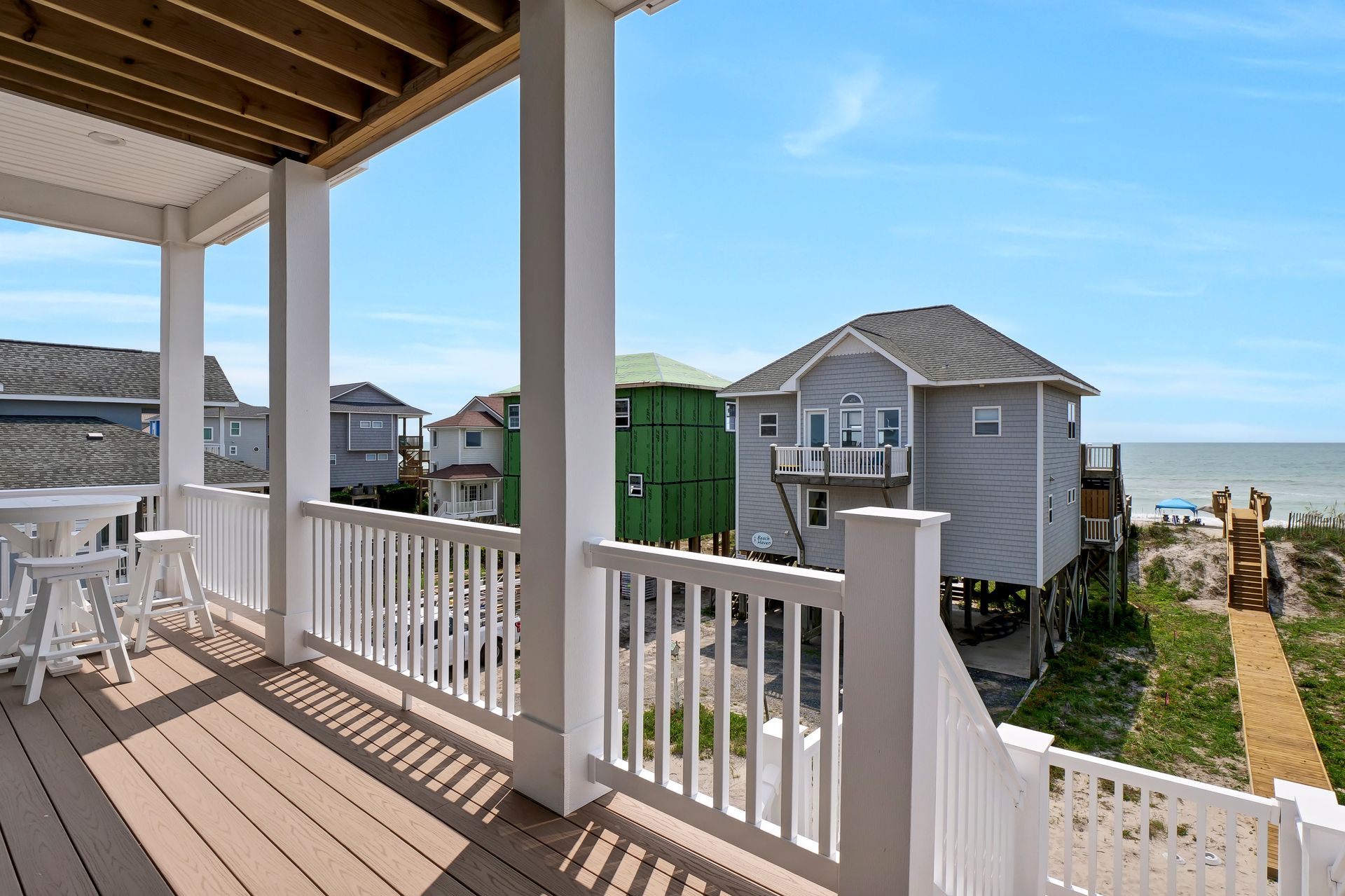 View from a porch overlooking beach houses and ocean under blue sky.