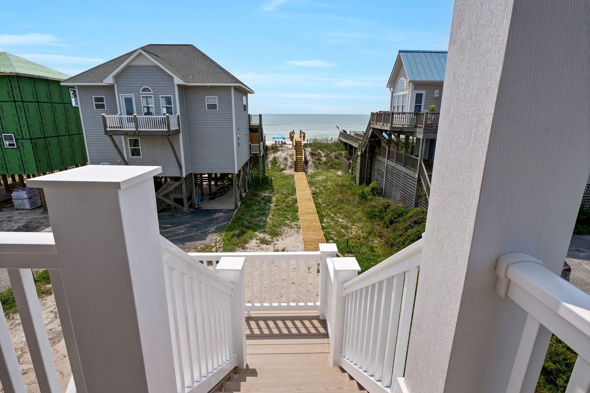Staircase leads to a beach path, flanked by houses under a blue sky.
