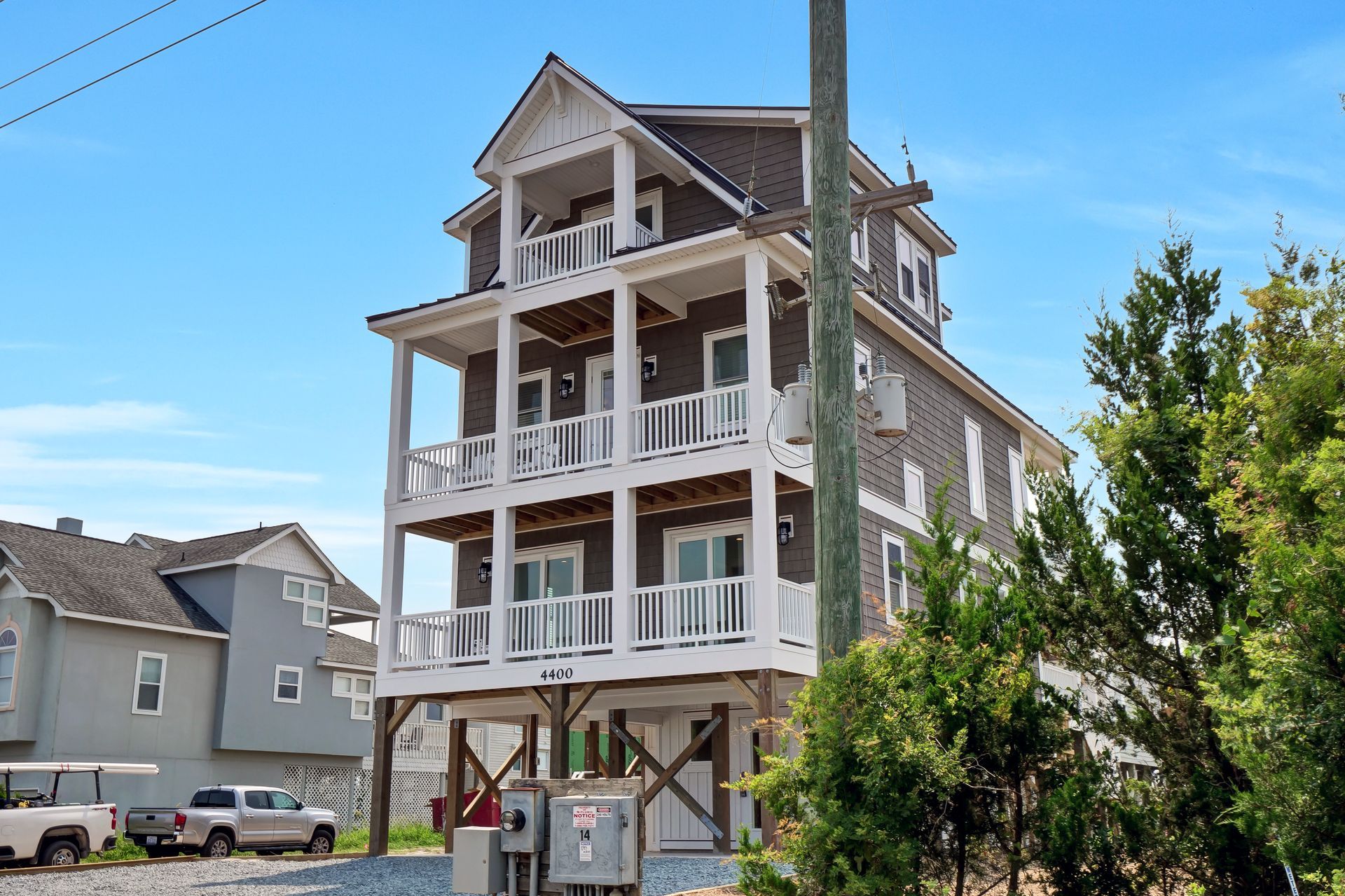 Multi-story beach house with brown siding, white balconies, and a blue sky.
