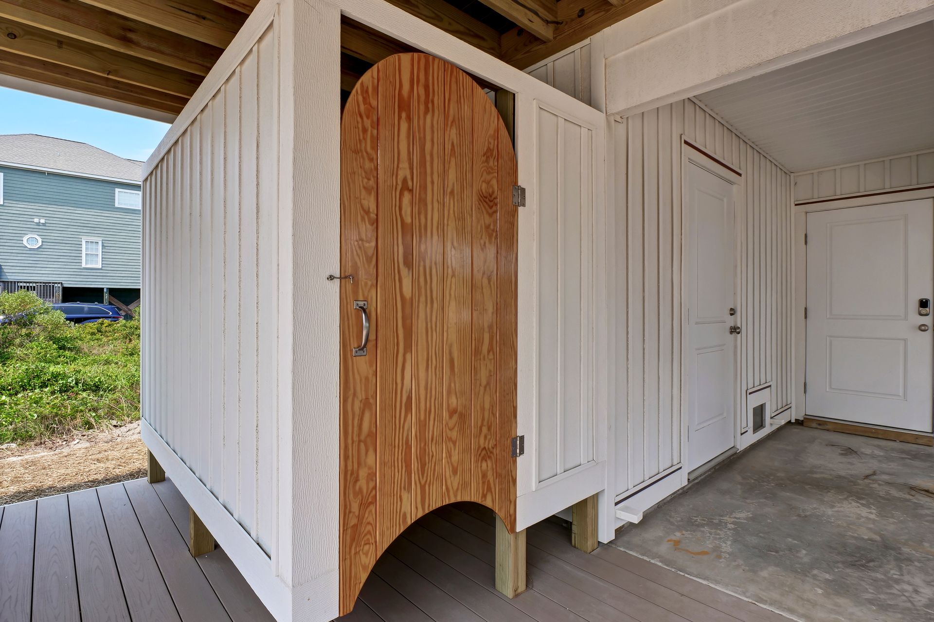 Outdoor wooden shower stall with arched wooden door and white siding.