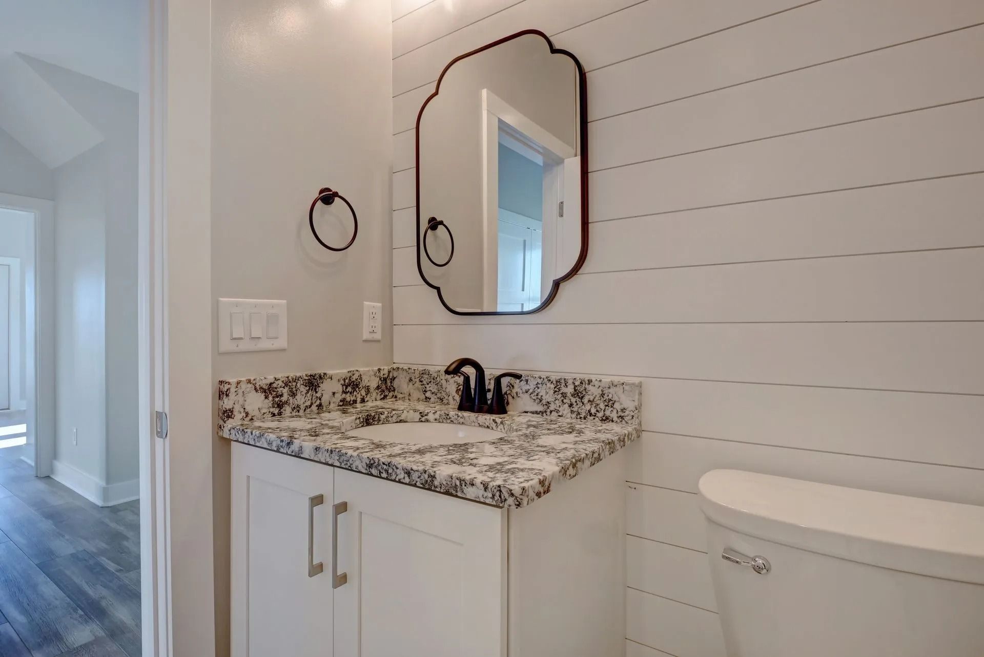 Bathroom with white vanity, black hardware, shiplap wall, and framed mirror.