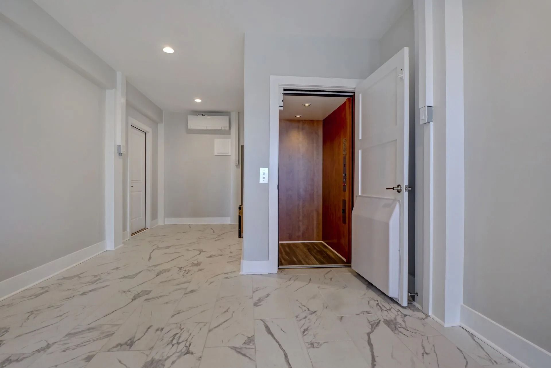 Hallway with an open elevator, marble flooring, and light gray walls.