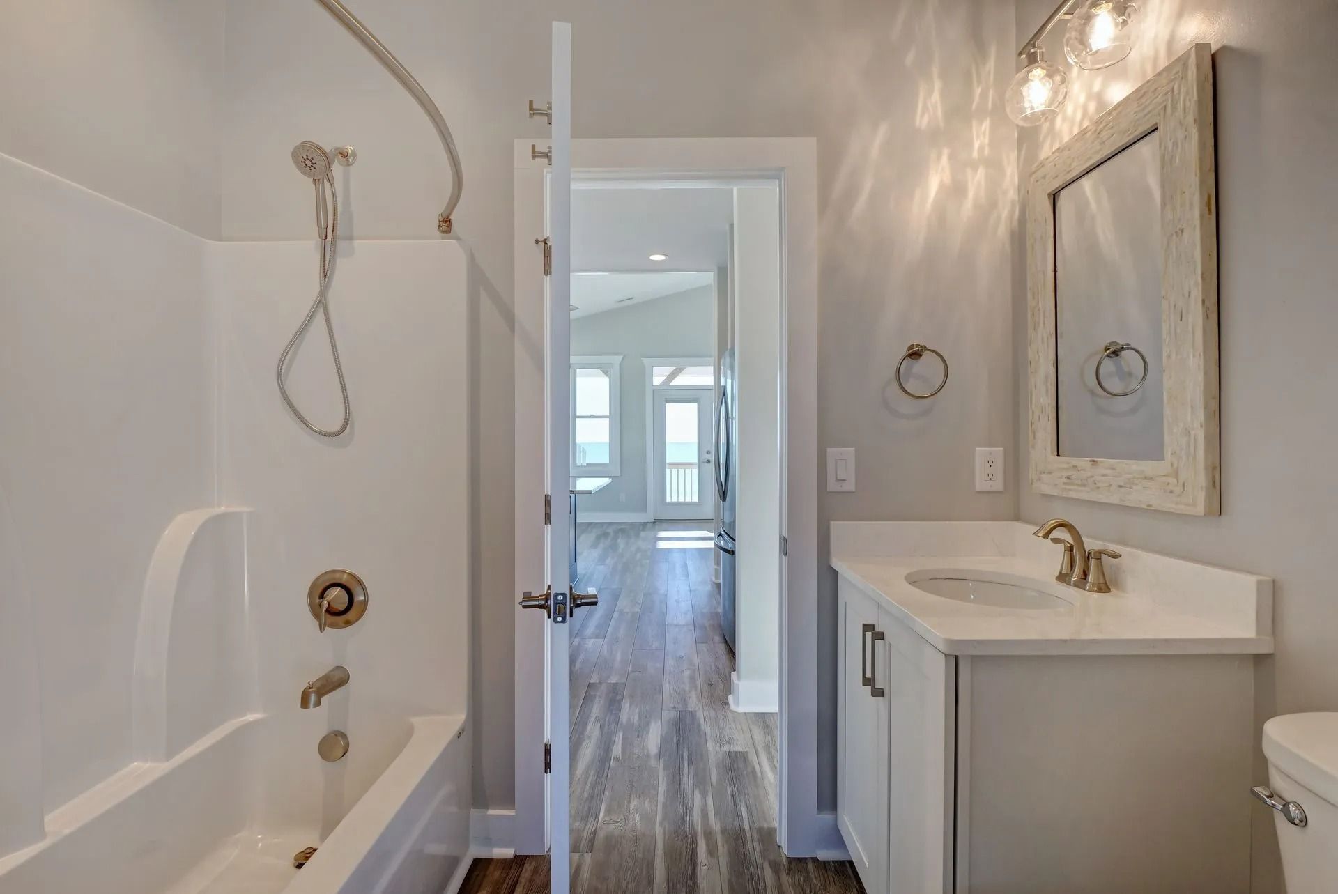 Bathroom with white tub, vanity, and open doorway to a living area with hardwood floors.