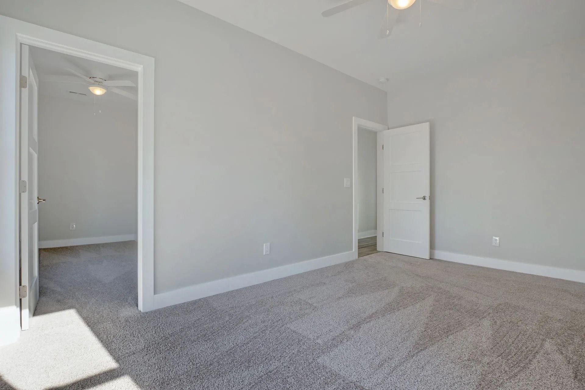 Empty bedroom with gray walls, carpet, and an open doorway to another room.