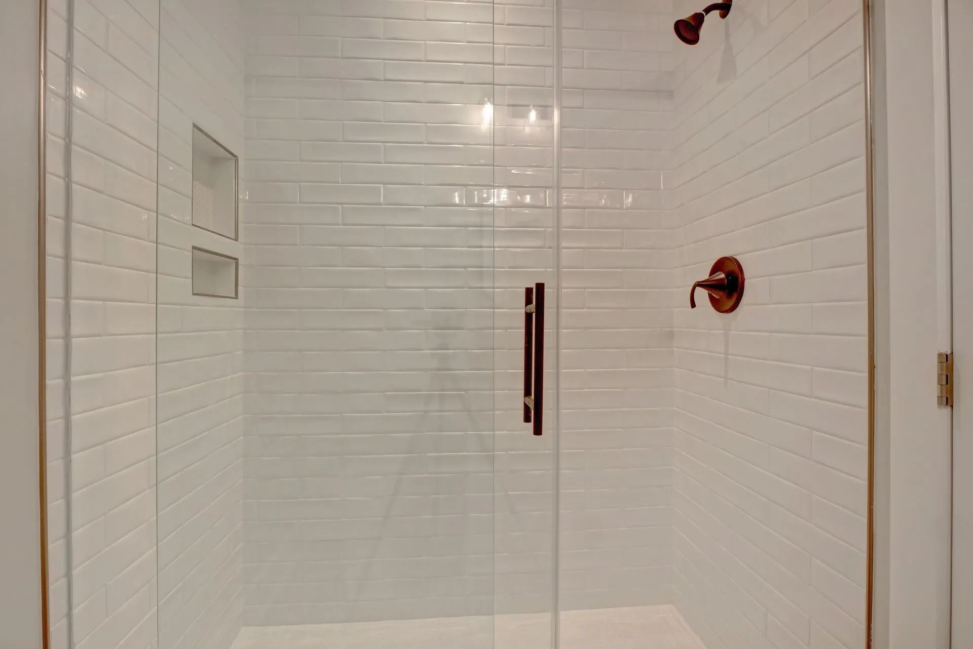 White tiled shower with glass door and bronze fixtures.