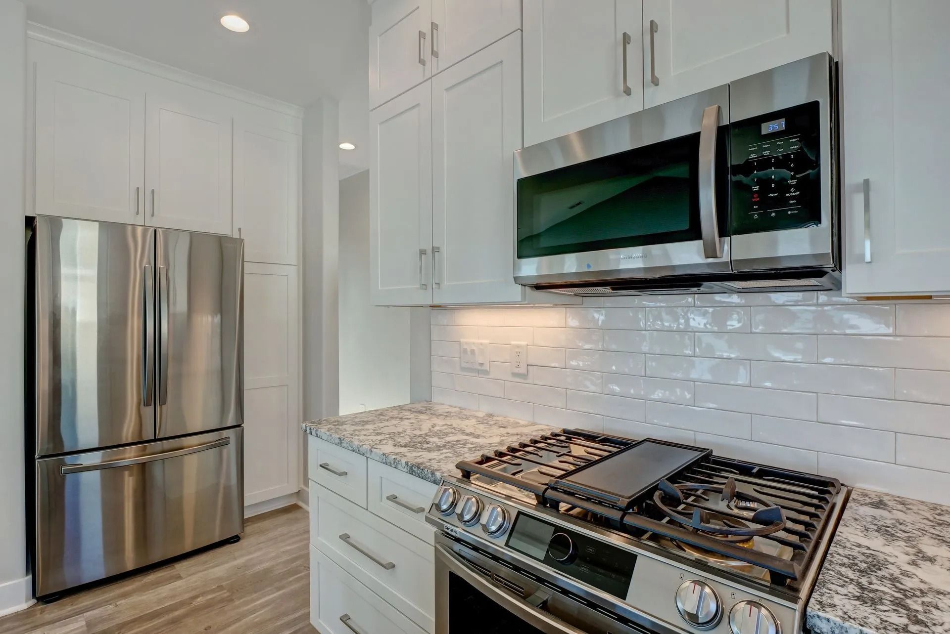 White kitchen with stainless steel appliances, white cabinets, and gas stovetop.
