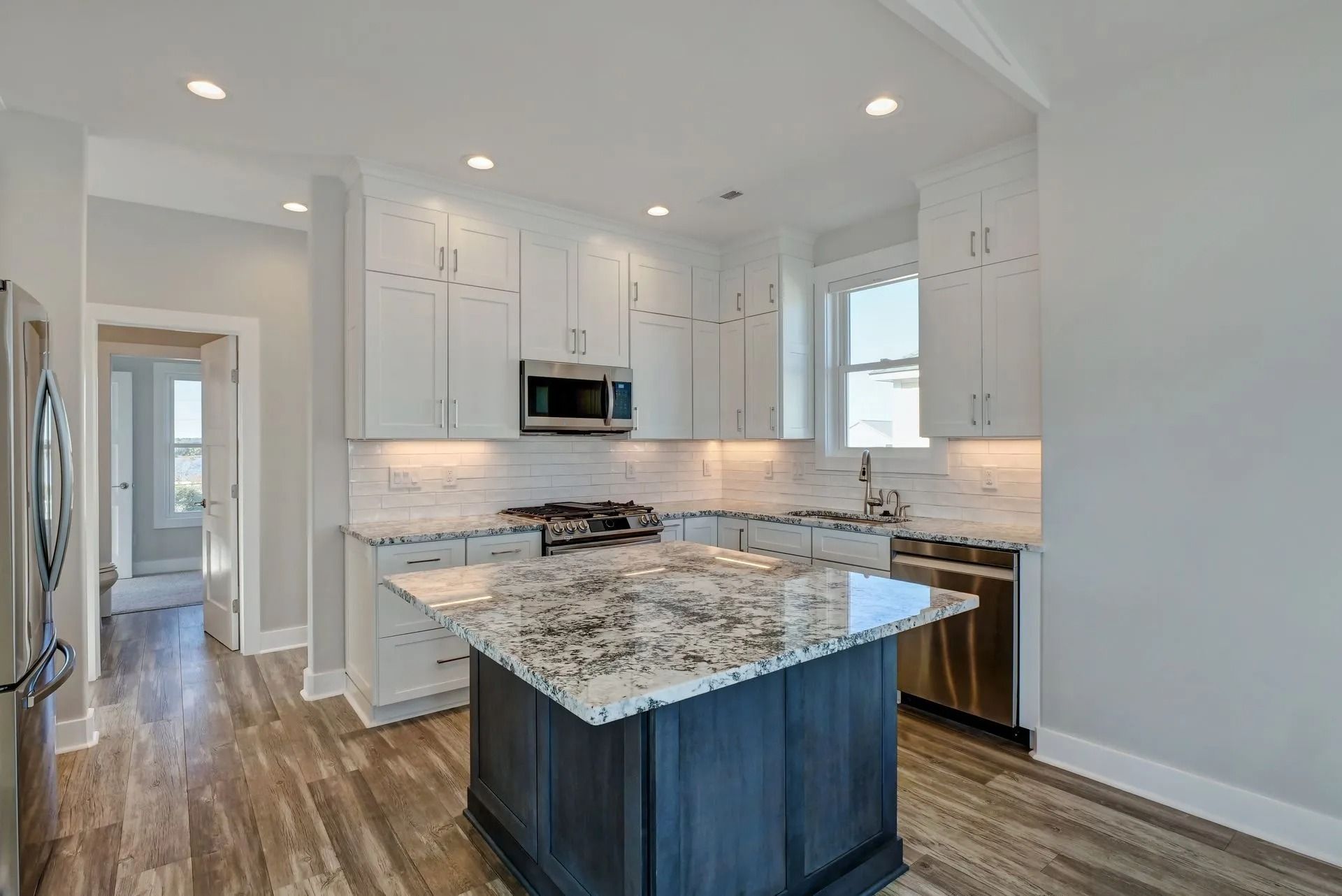 Kitchen with white cabinets, dark blue island, and granite countertops.