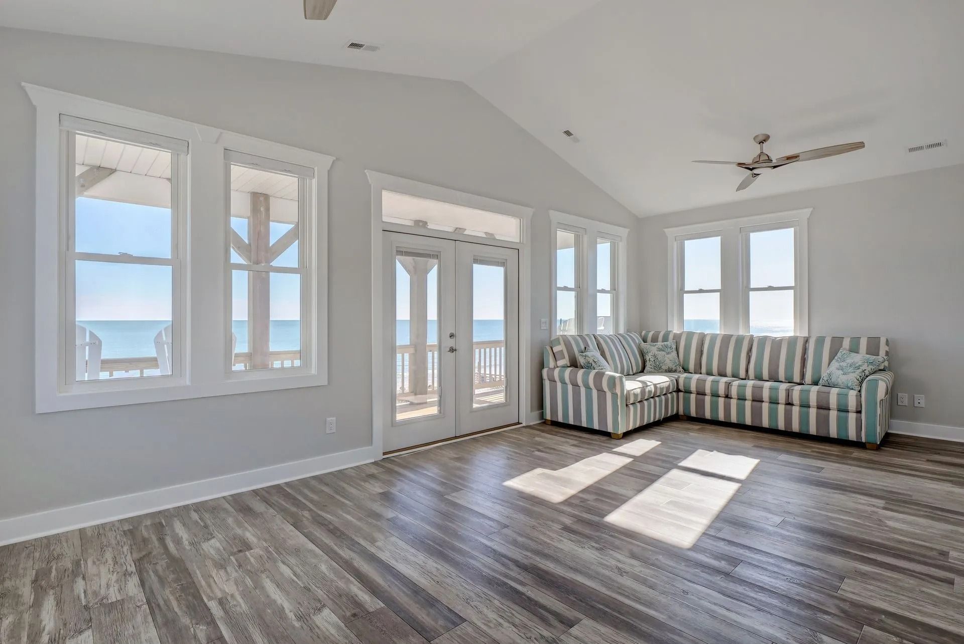 Spacious living room with ocean view, striped sofa, hardwood floors, and large windows.