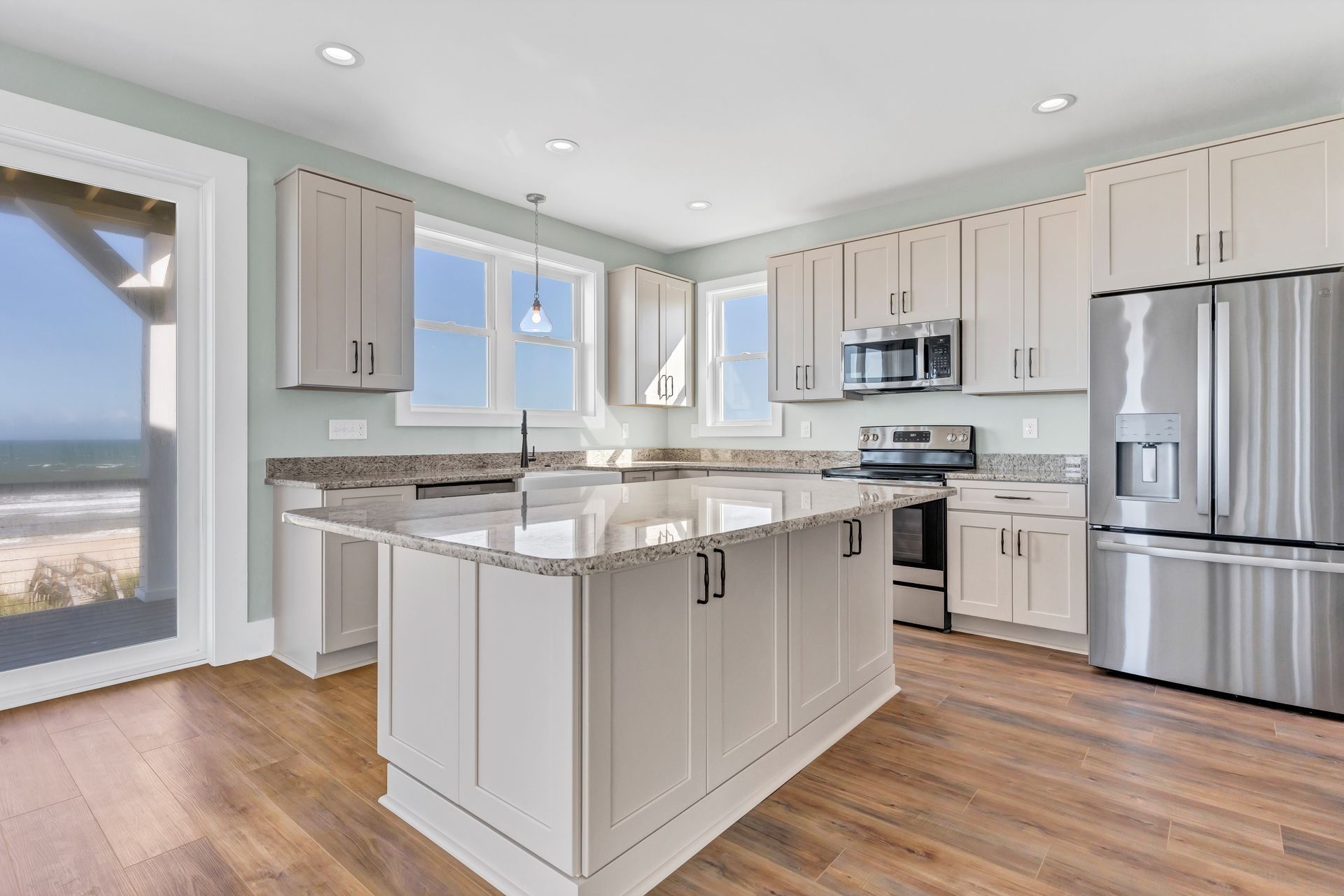 Kitchen with island, light cabinets, stainless steel appliances, and ocean view through a window.