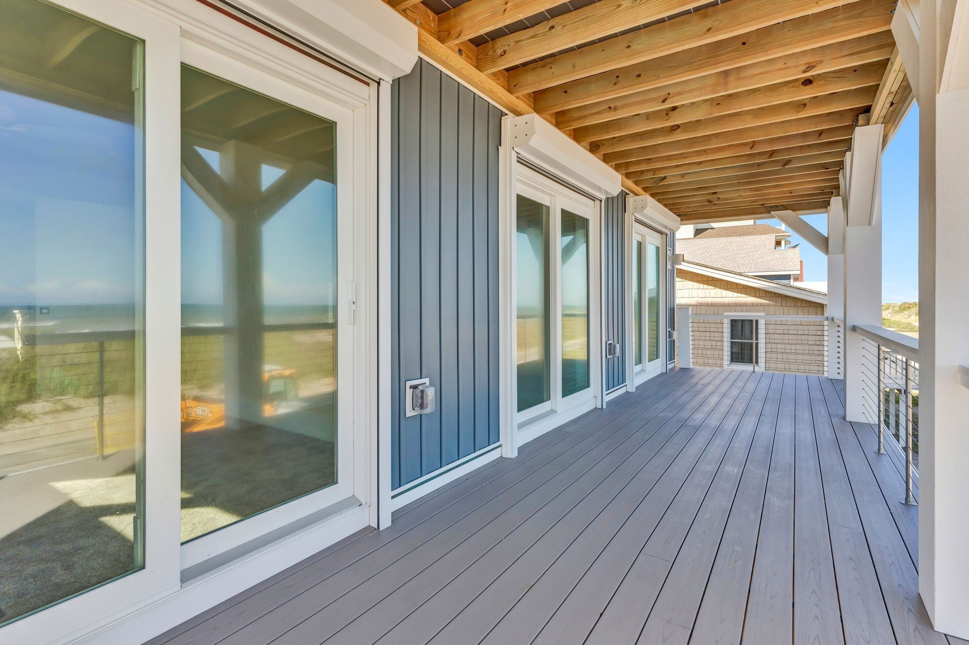 Blue-sided beach house with deck overlooking the ocean. Glass doors and windows. Gray deck and white trim.